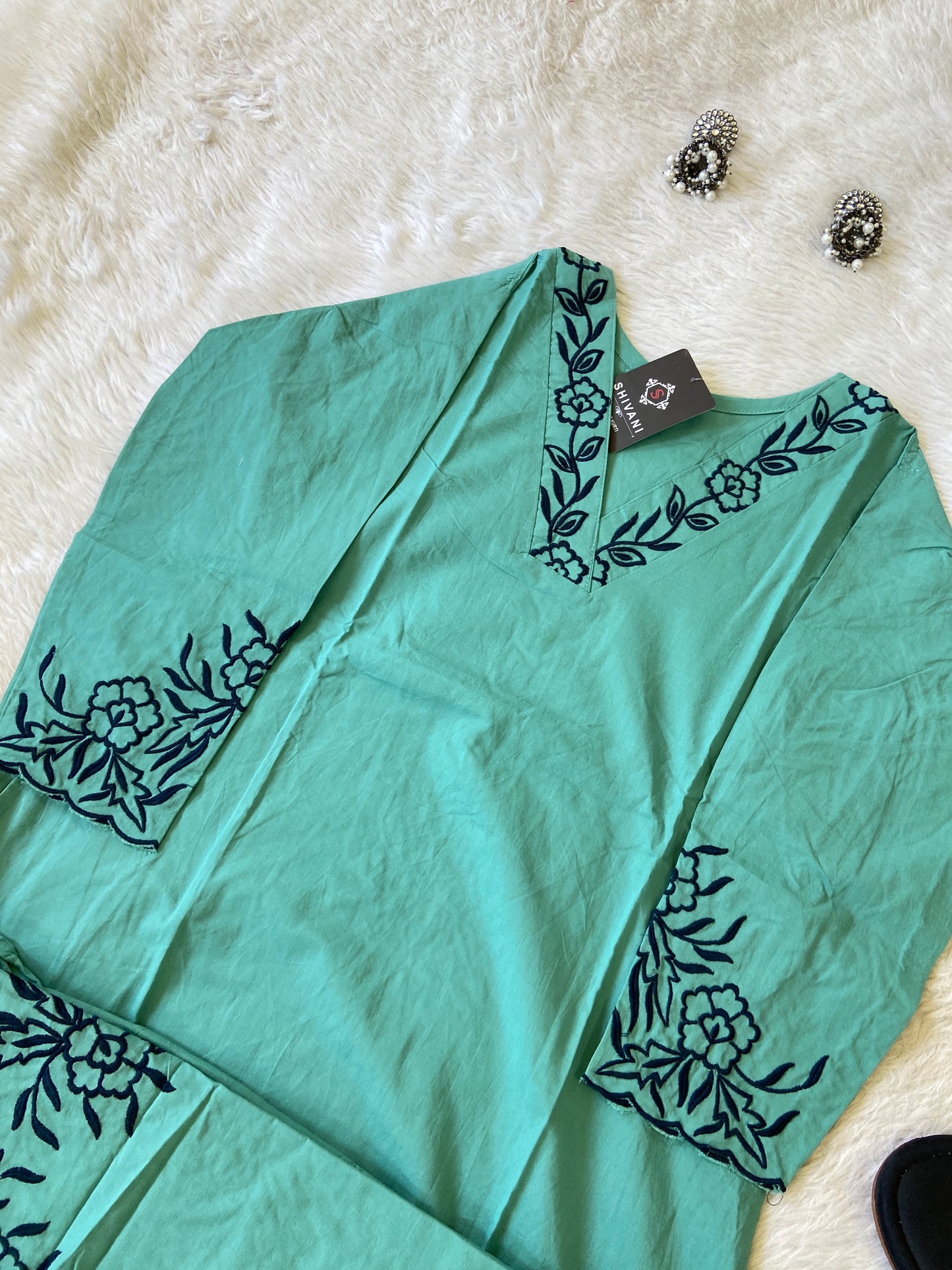 Teal top with black floral embroidery on a white fur surface