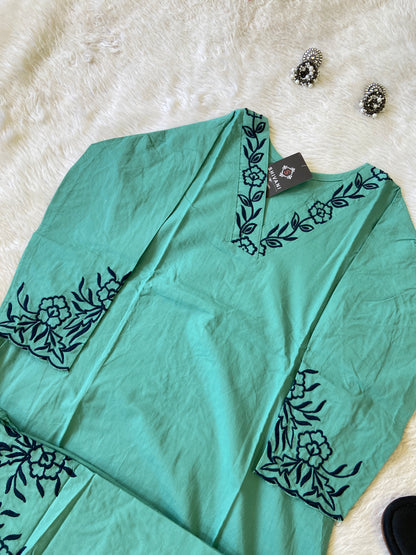 Teal top with black floral embroidery on a white fur surface