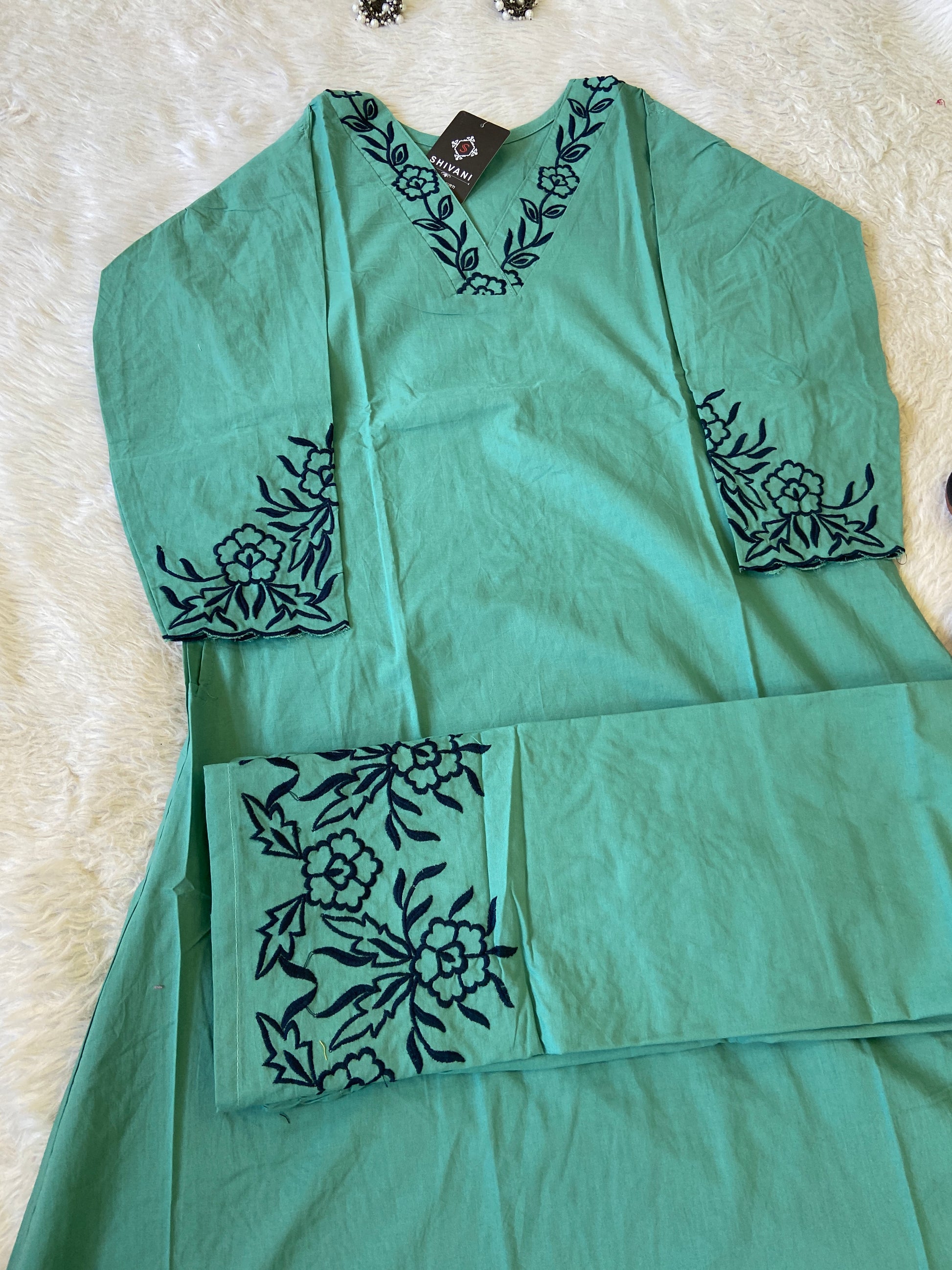 Green fabric with black floral embroidery on a textured surface