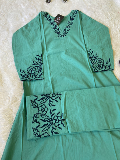 Green fabric with black floral embroidery on a textured surface