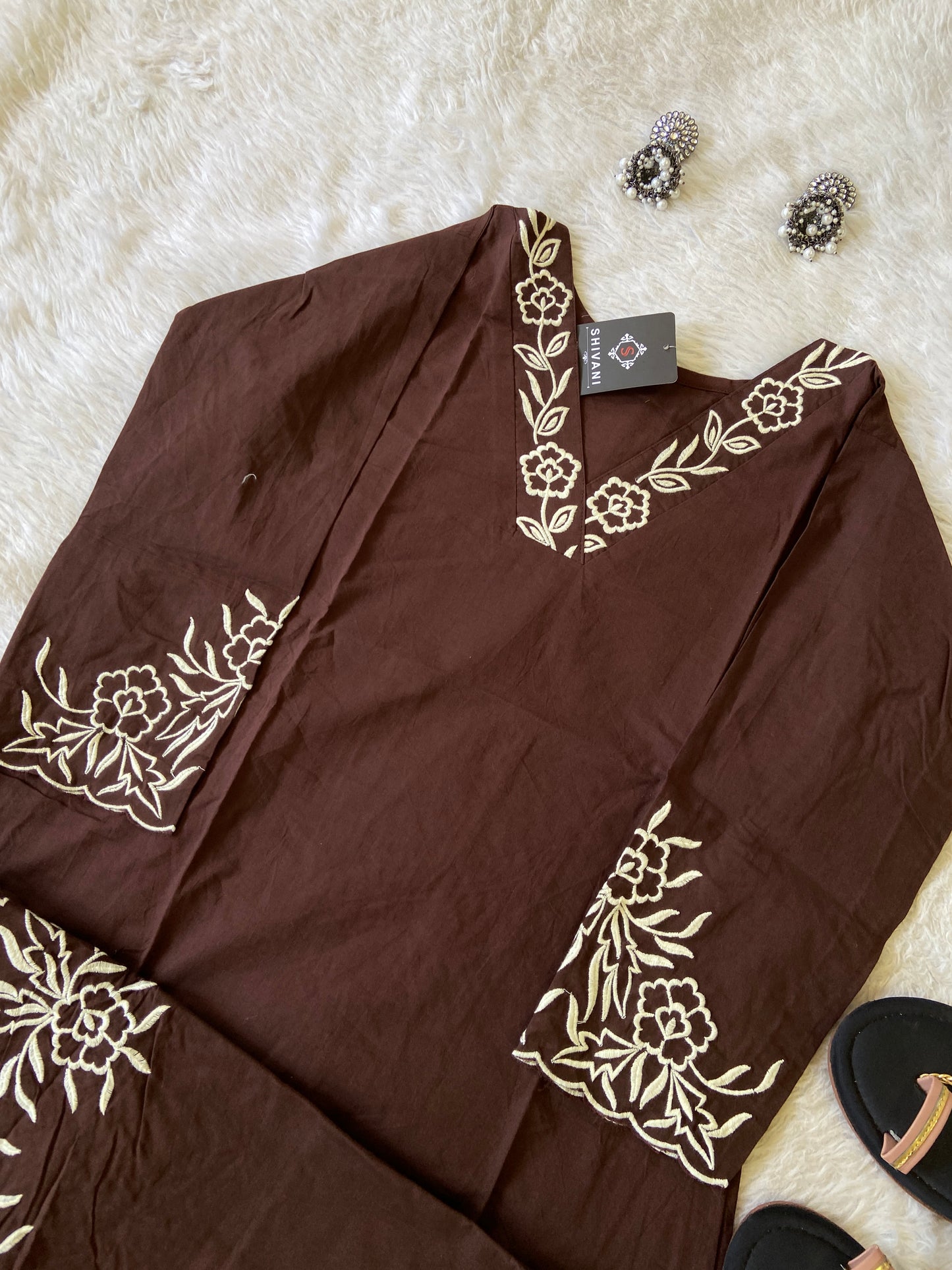 Brown fabric with white floral embroidery on a white surface, with a 'Shivan' tag visible.