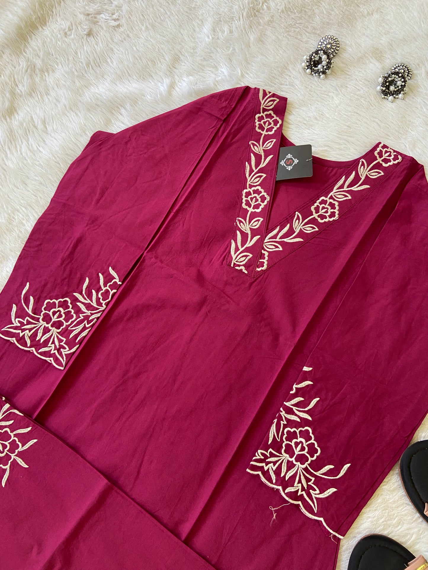 Maroon garment with white floral embroidery on a white surface