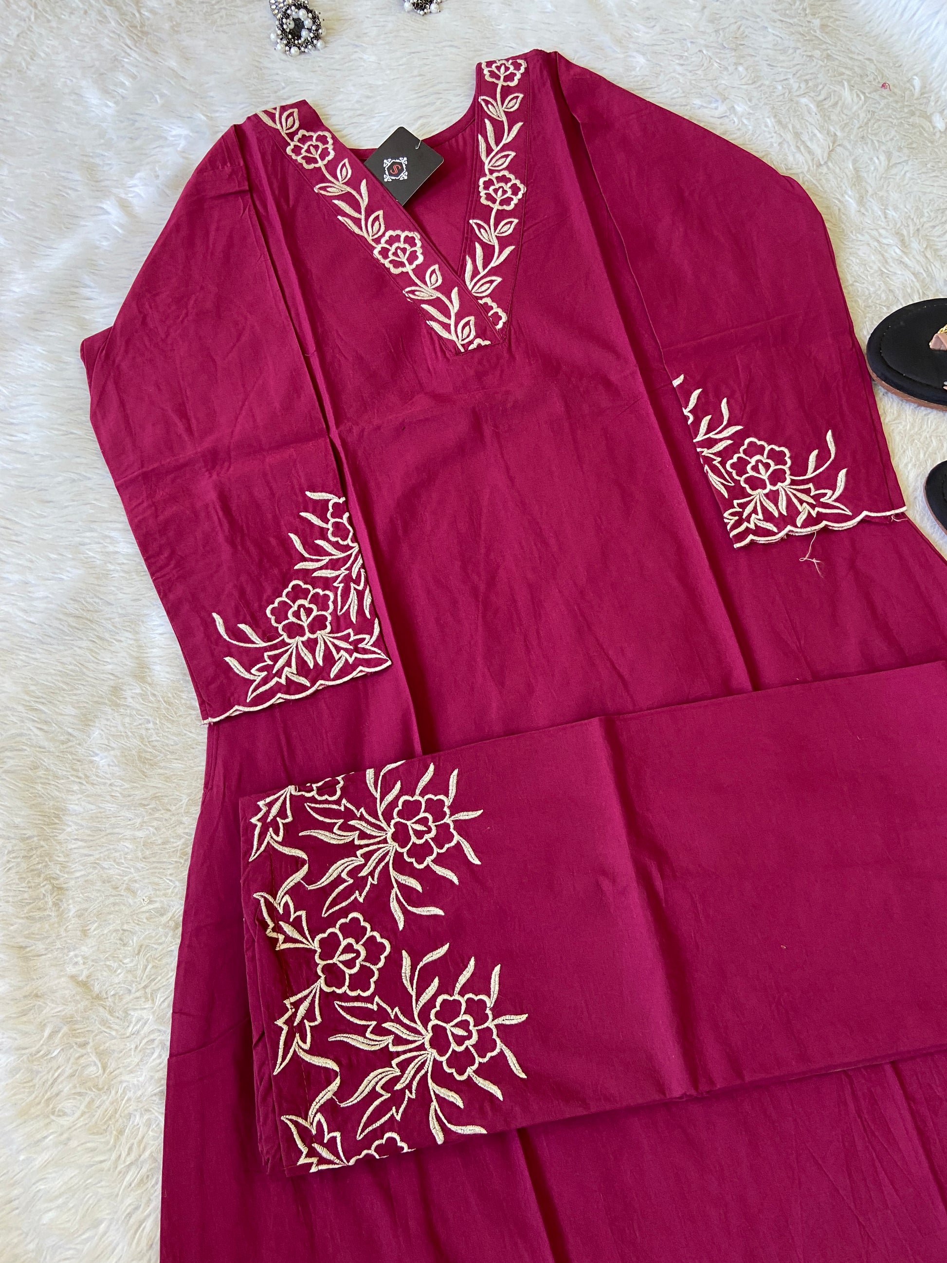 Maroon fabric with white floral embroidery on a textured surface