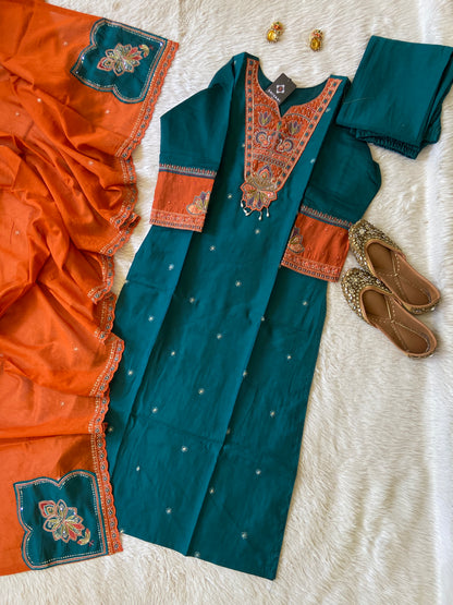 Teal and orange traditional outfit with embroidered details on a textured white surface.