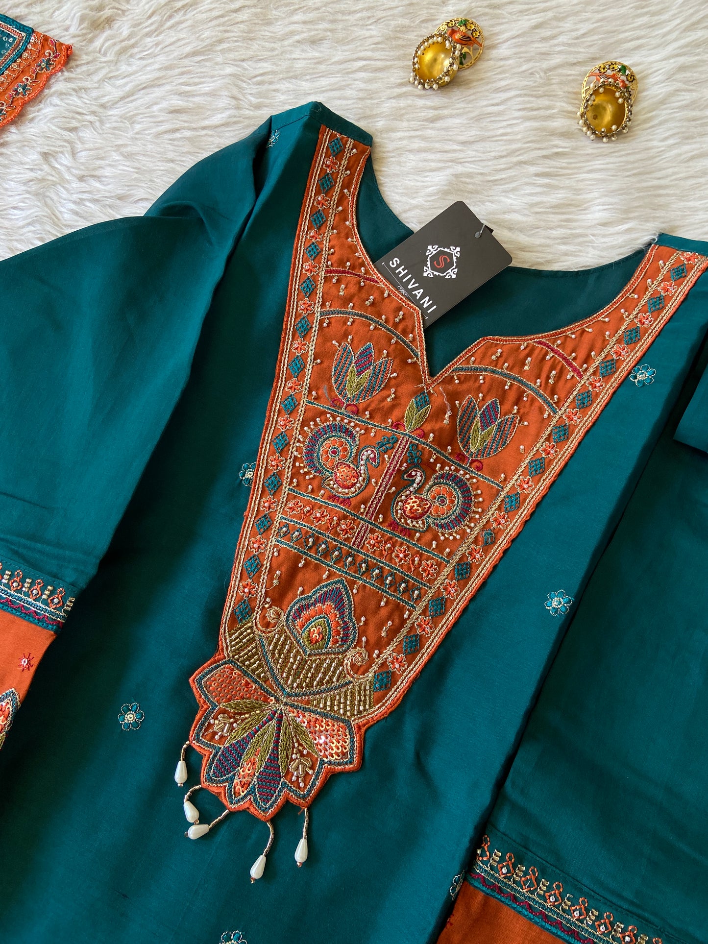 Teal fabric with intricate orange embroidery on a white surface