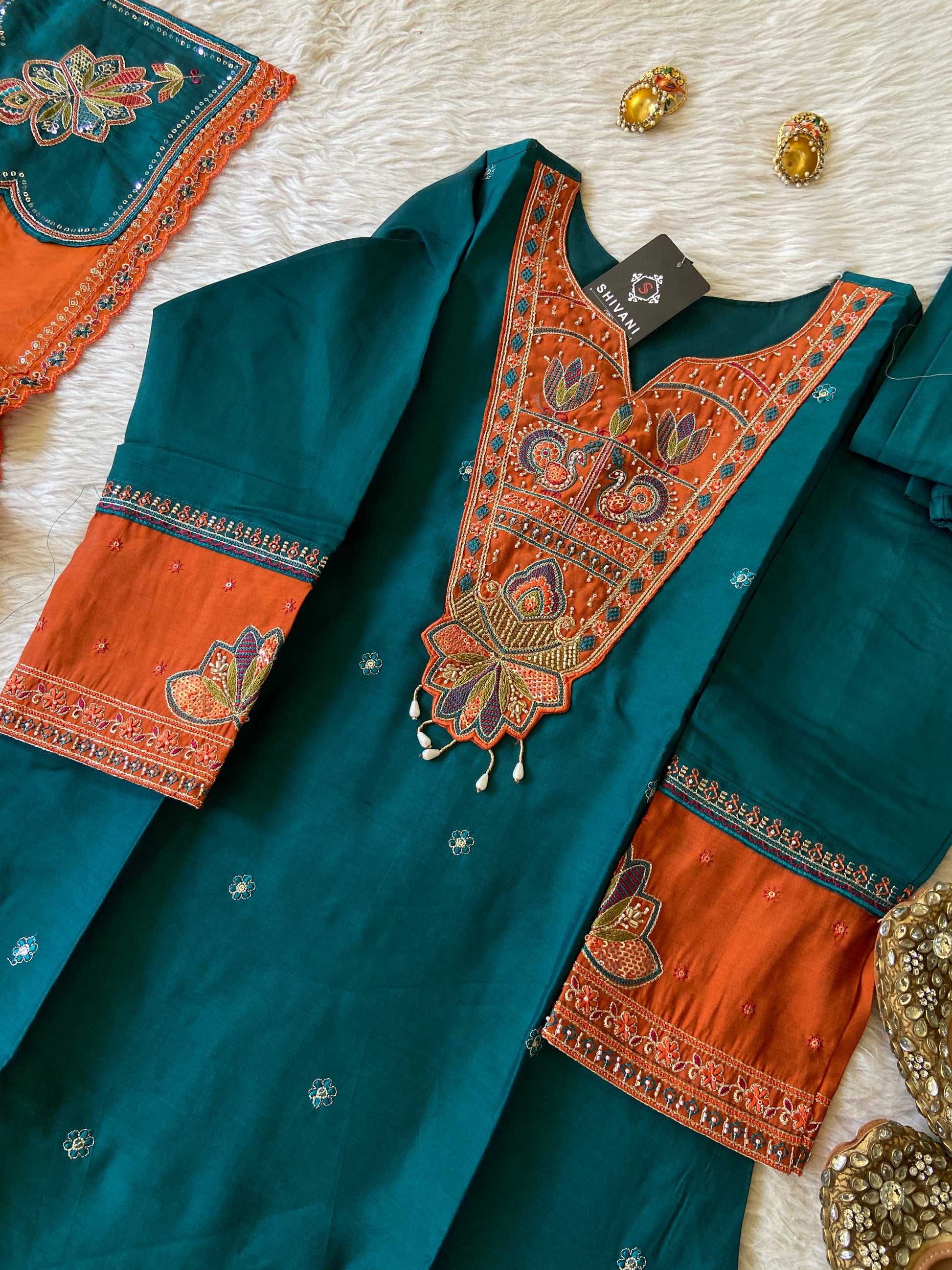 Teal and orange traditional outfit with intricate embroidery on a textured surface