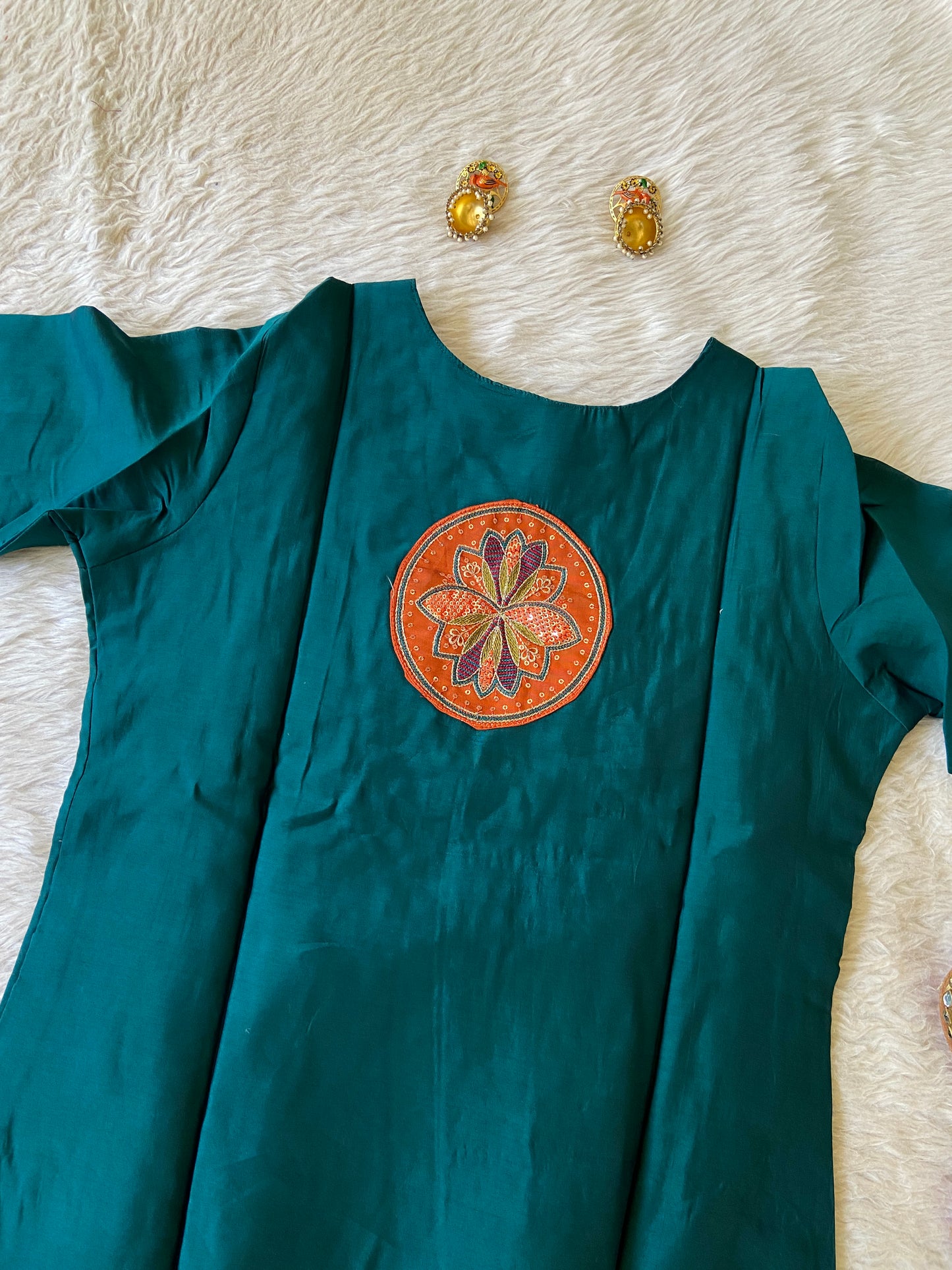 Teal fabric with a decorative orange emblem on a textured white surface