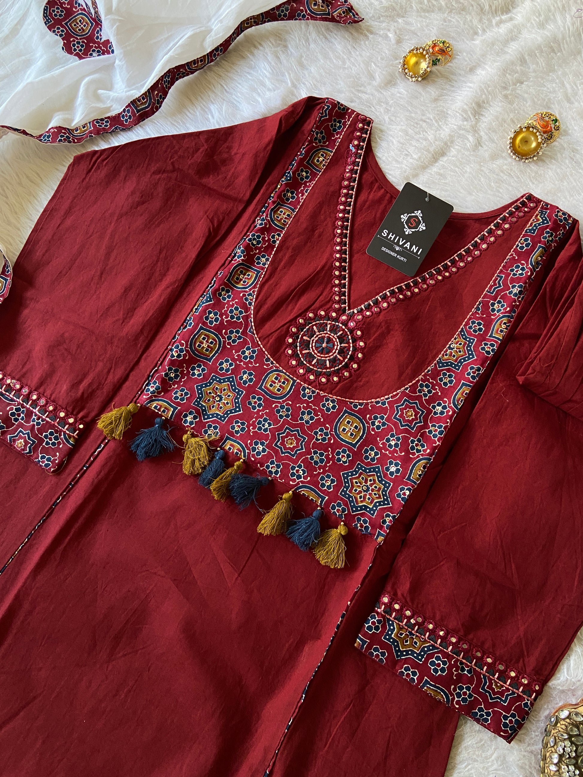 Maroon embroidered garment with decorative elements on a white surface