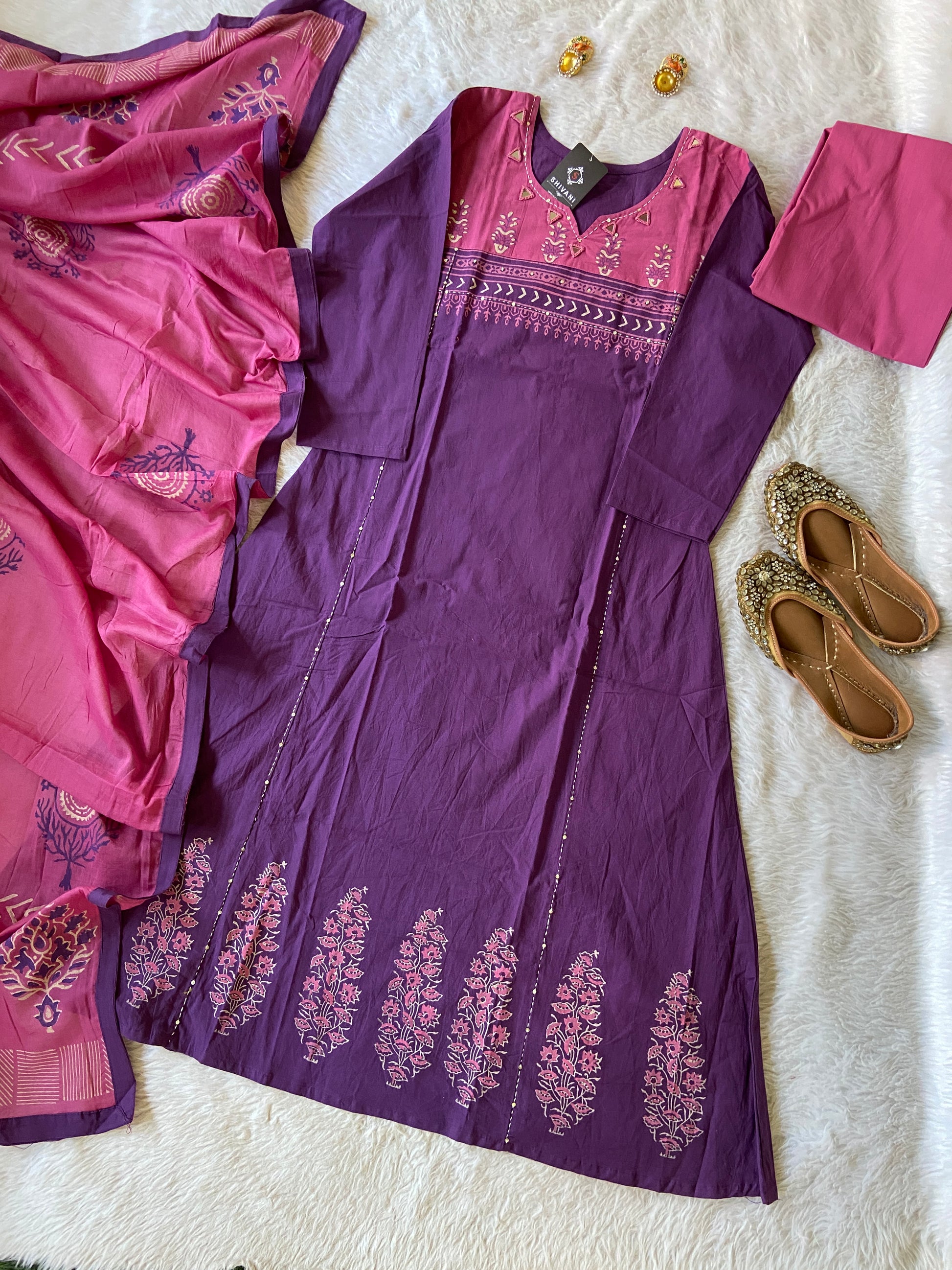 Purple dress with pink accents on a white surface, surrounded by pink fabric and sandals.