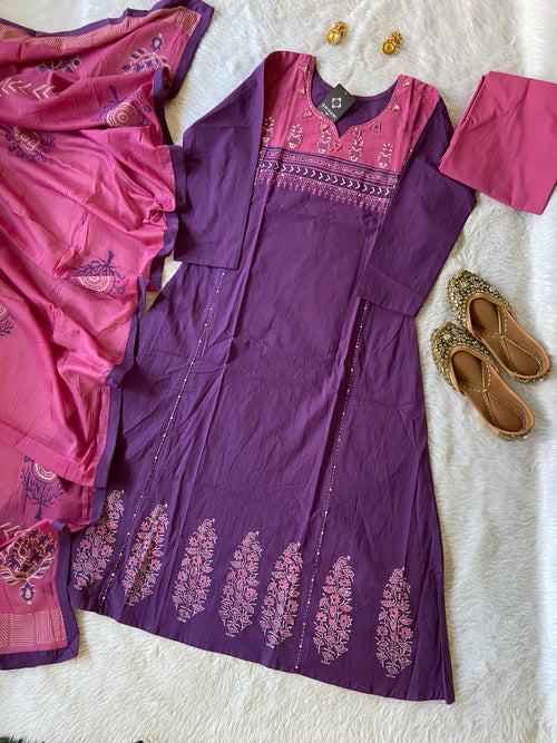 Purple dress with pink accents on a white surface, surrounded by pink fabric and sandals.