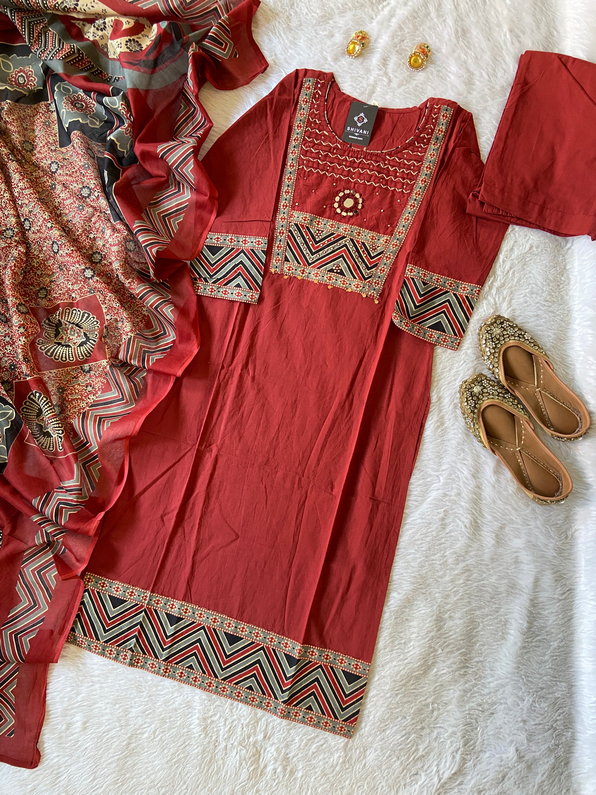 Red embroidered traditional outfit with a patterned shawl on a white surface.