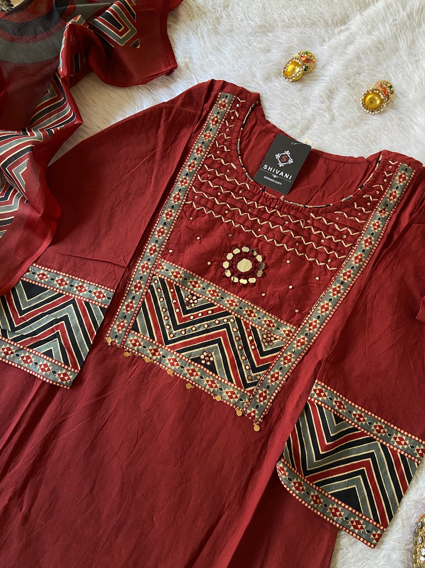 Maroon embroidered garment with geometric patterns on a white surface