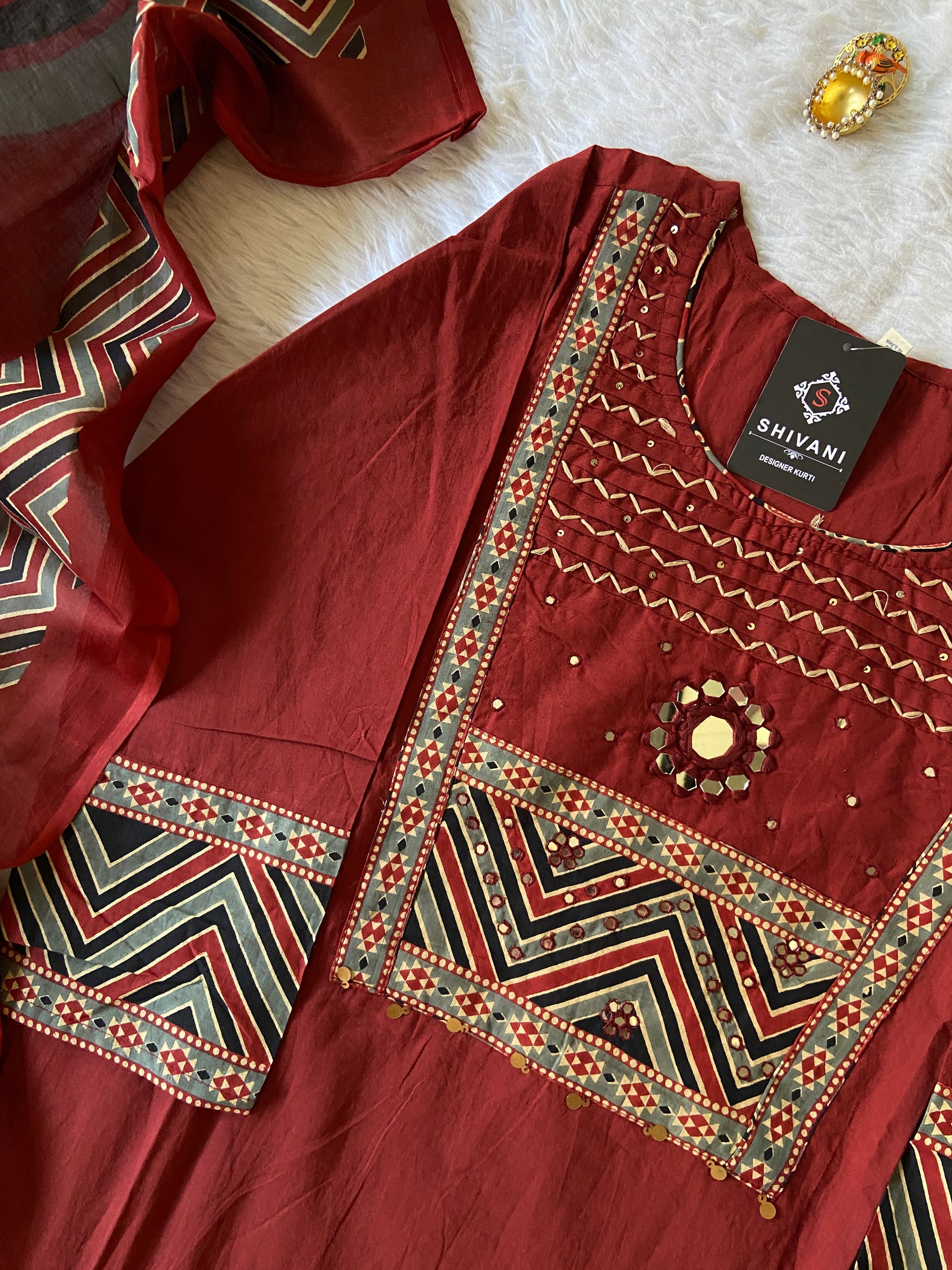 Maroon fabric with intricate patterns and a brand tag on a white surface