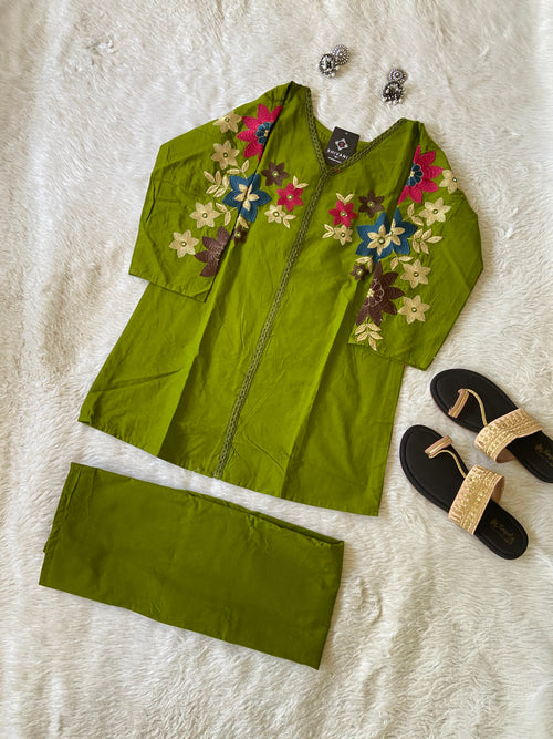 Green embroidered outfit with floral patterns on a textured white surface