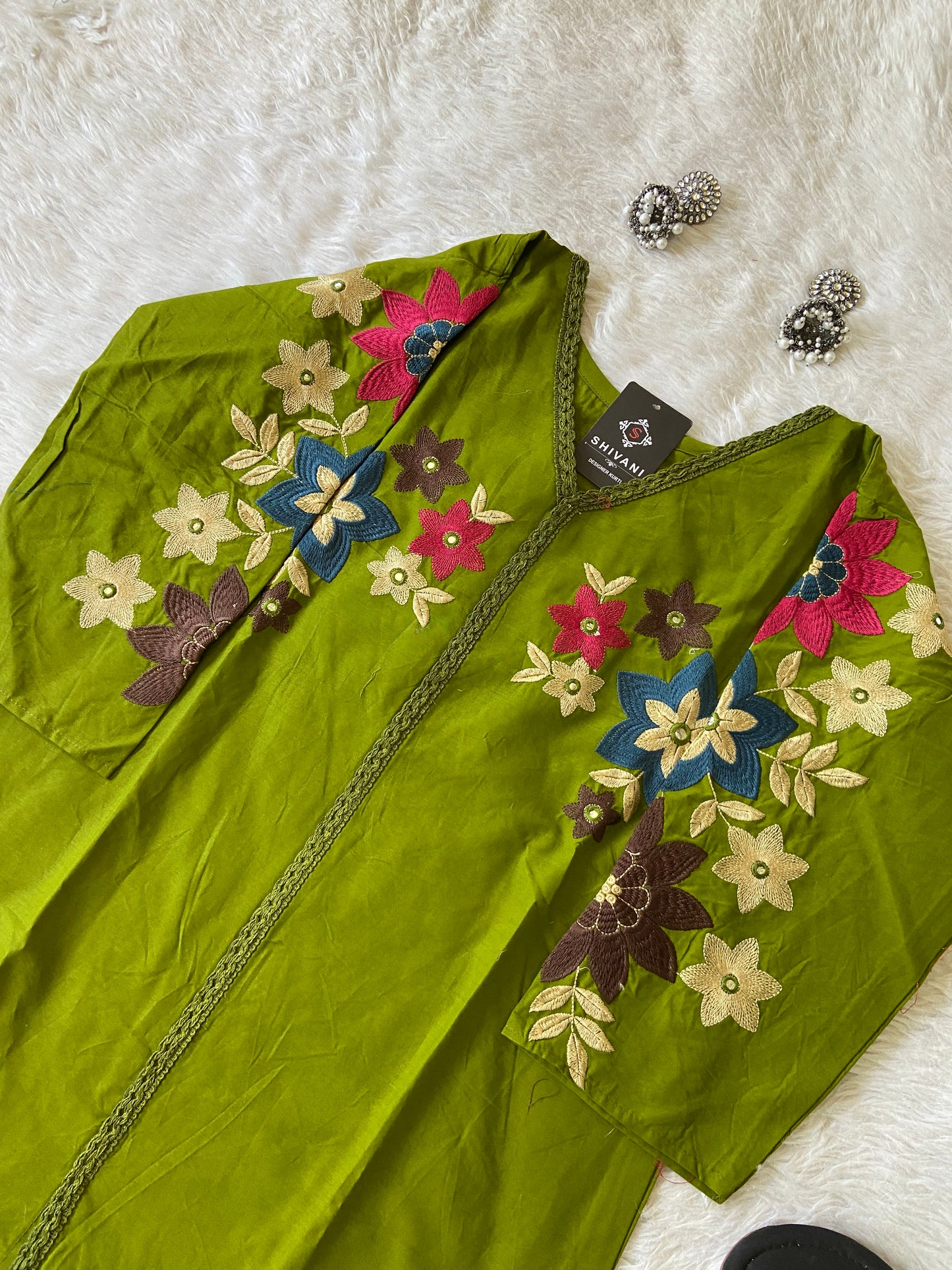 Green embroidered garment with colorful flowers on a white surface