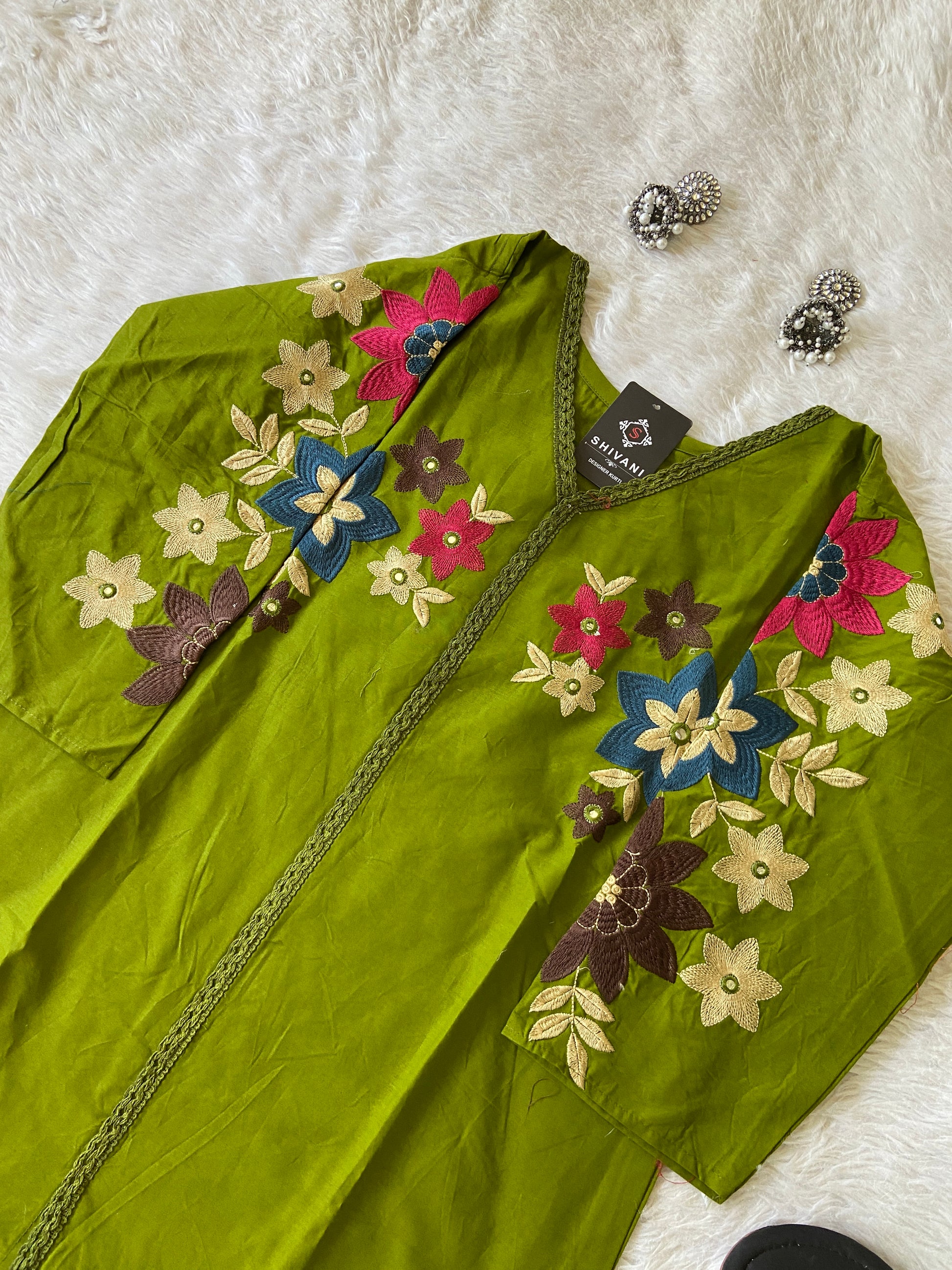 Green embroidered garment with colorful flowers on a white surface