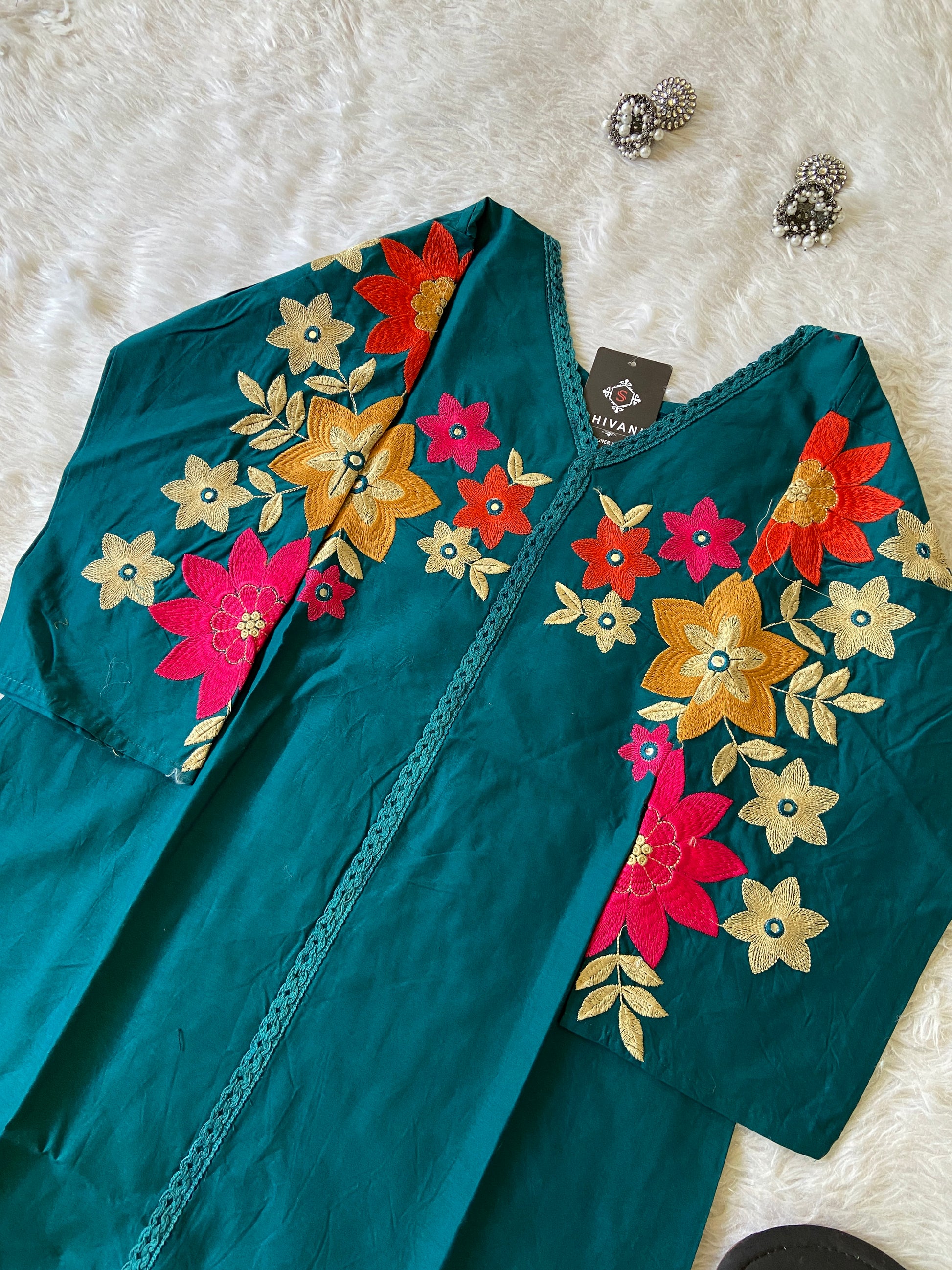 Teal fabric with colorful floral embroidery on a white surface