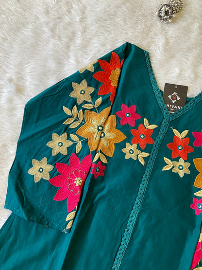 Teal dress with colorful floral embroidery on a white fur background
