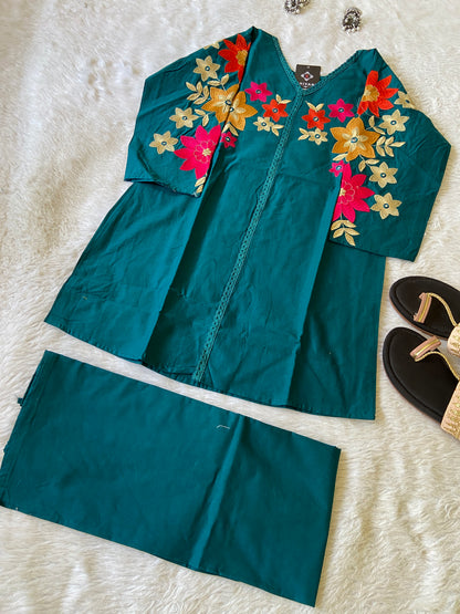 Teal outfit with floral embroidery on a white textured surface