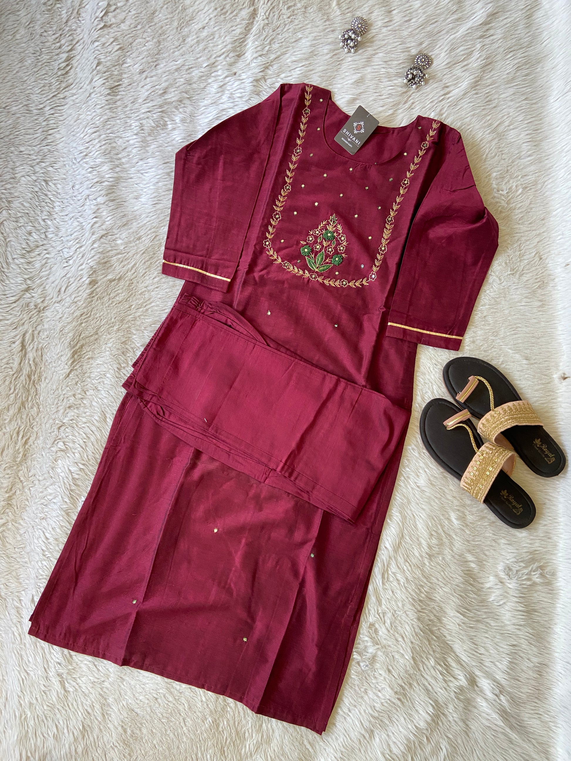 Maroon traditional outfit with embroidery on a white textured surface, accompanied by sandals.