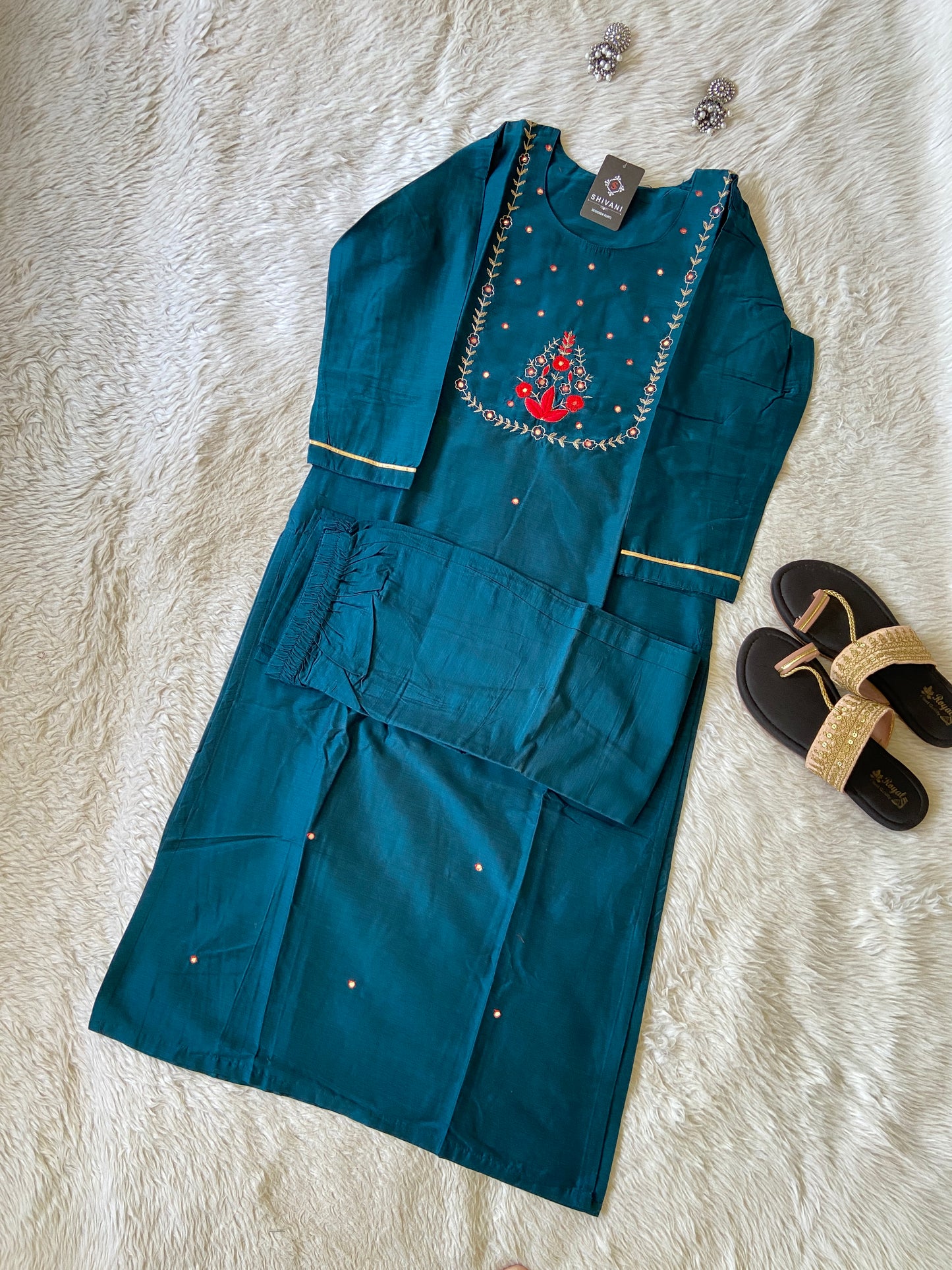 Blue embroidered garment on a textured white surface with sandals in the background
