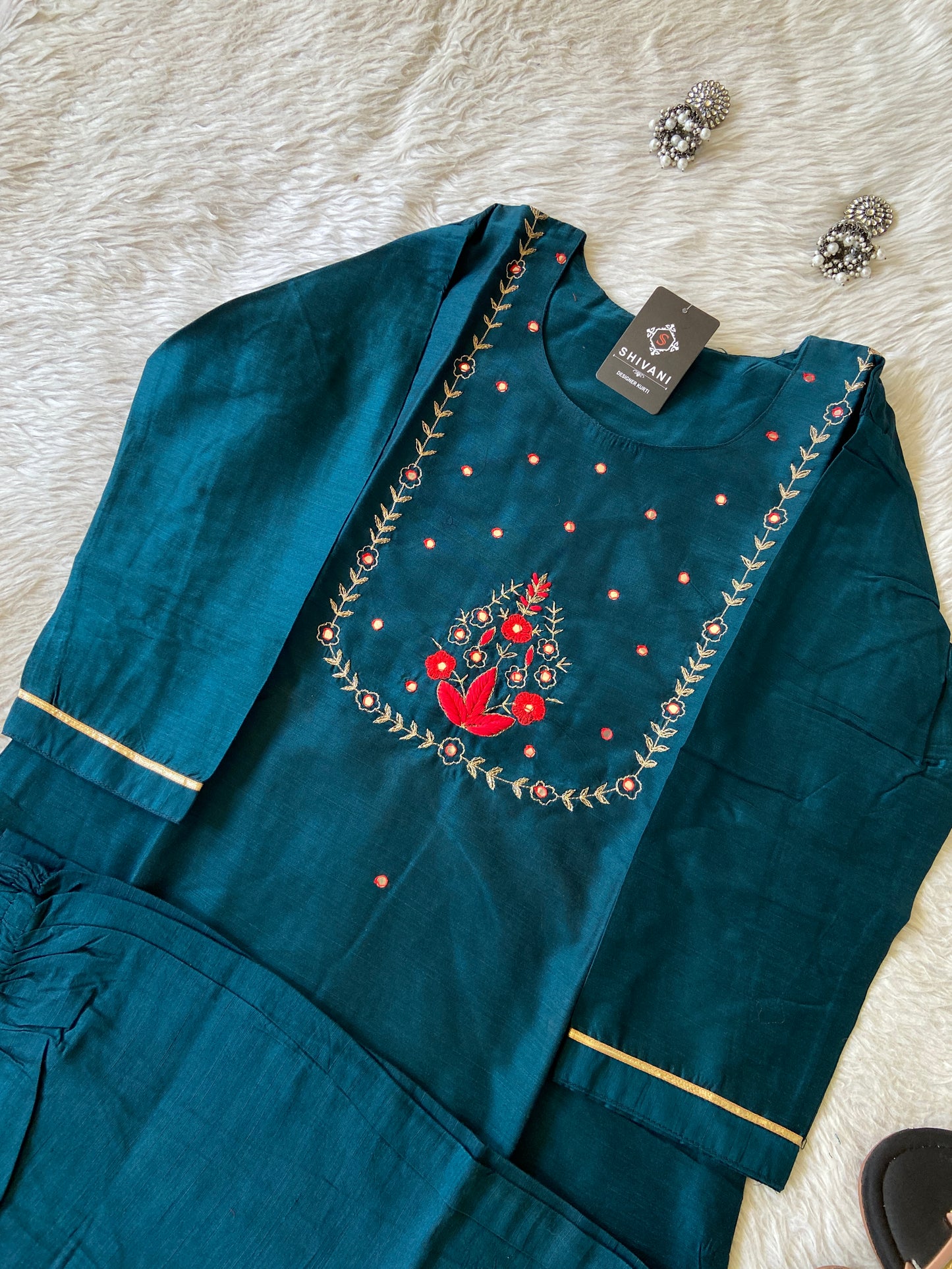 Teal embroidered garment with a red bird design on a white surface