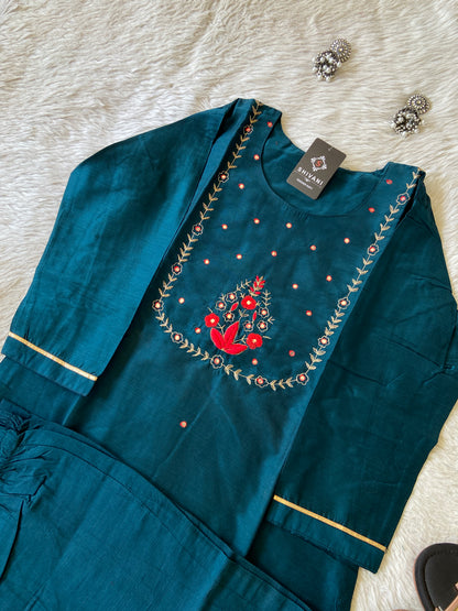 Teal embroidered garment with a red bird design on a white surface