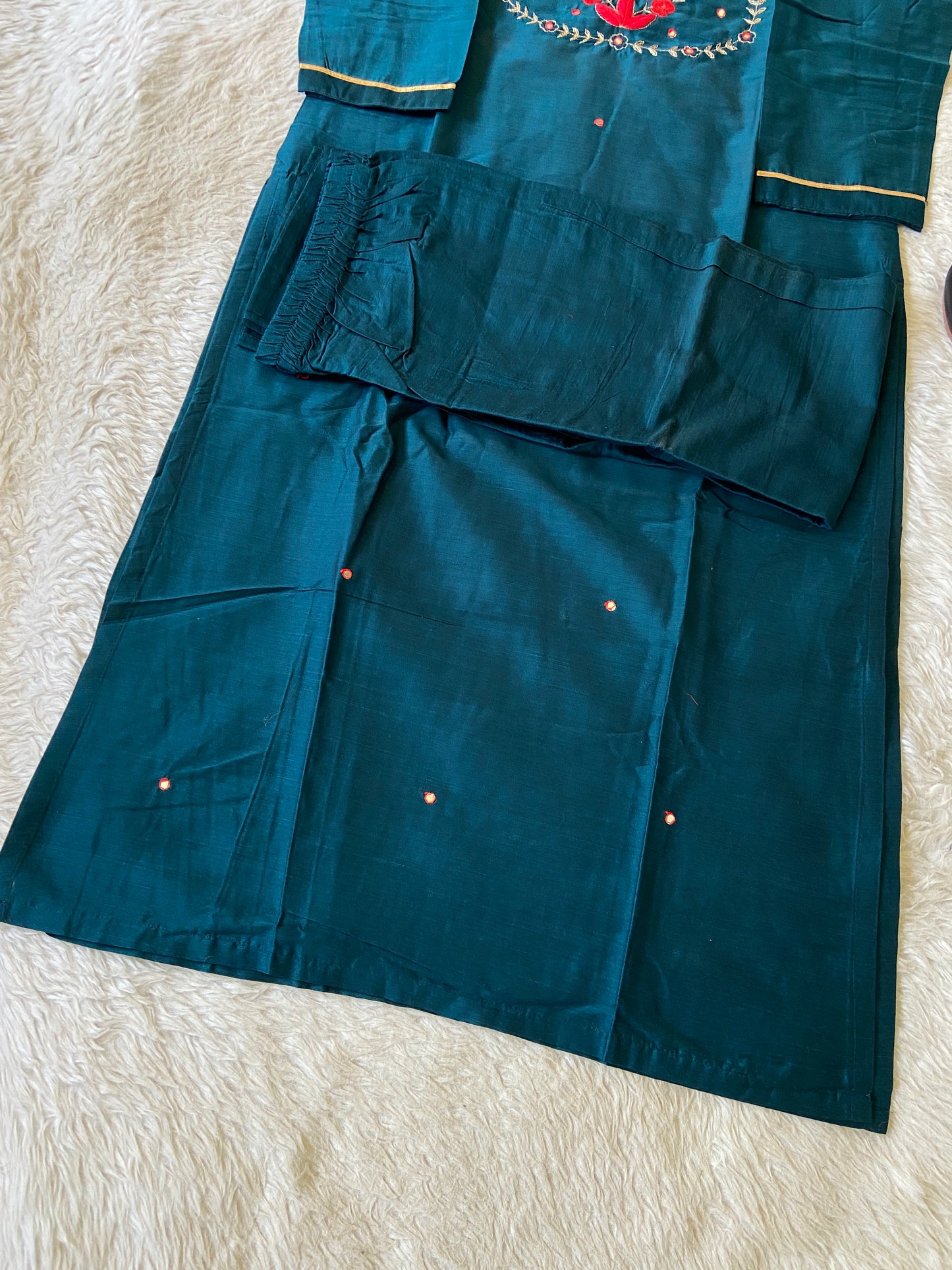 Teal fabric with red embroidery on a beige surface