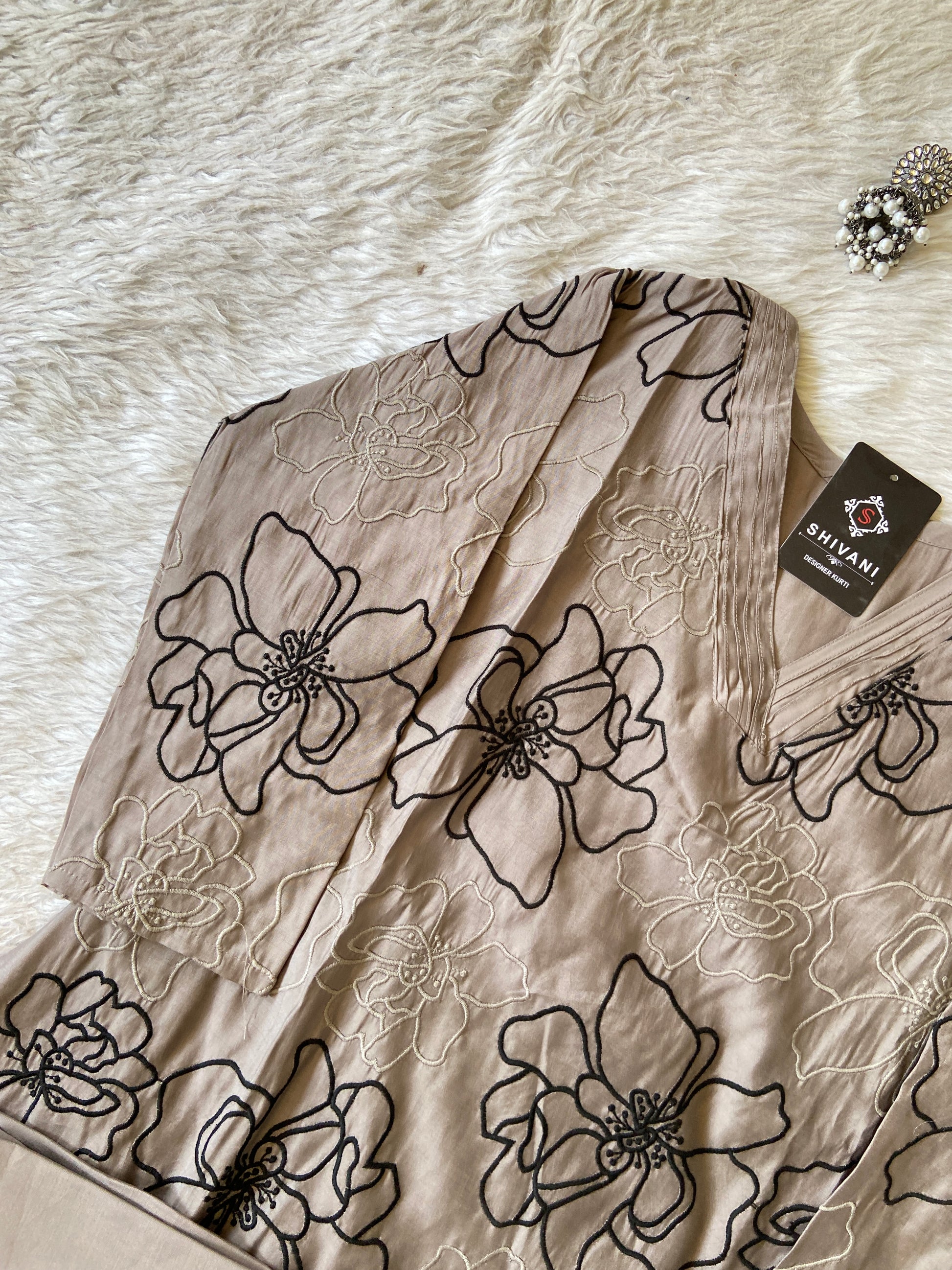 Beige fabric with black floral embroidery on a white surface