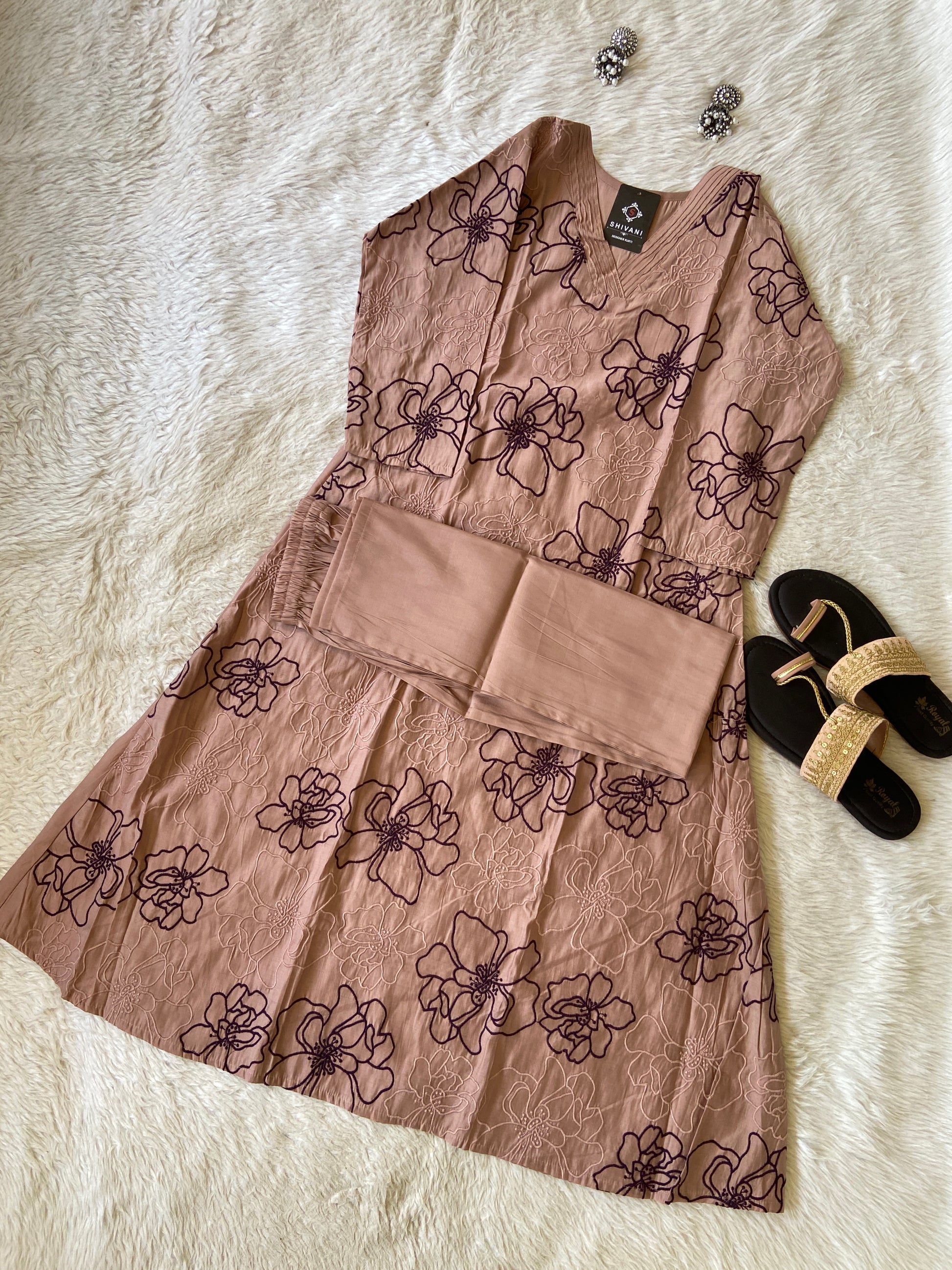 Floral-patterned dress on a white fur surface with sandals and a belt.