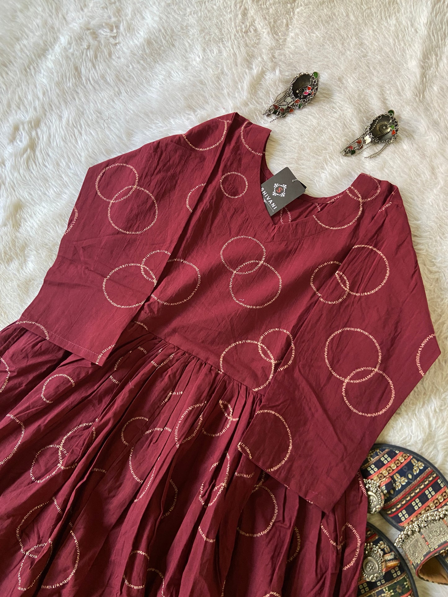 Red dress with gold circle pattern on a white textured surface with earrings and a decorative item.