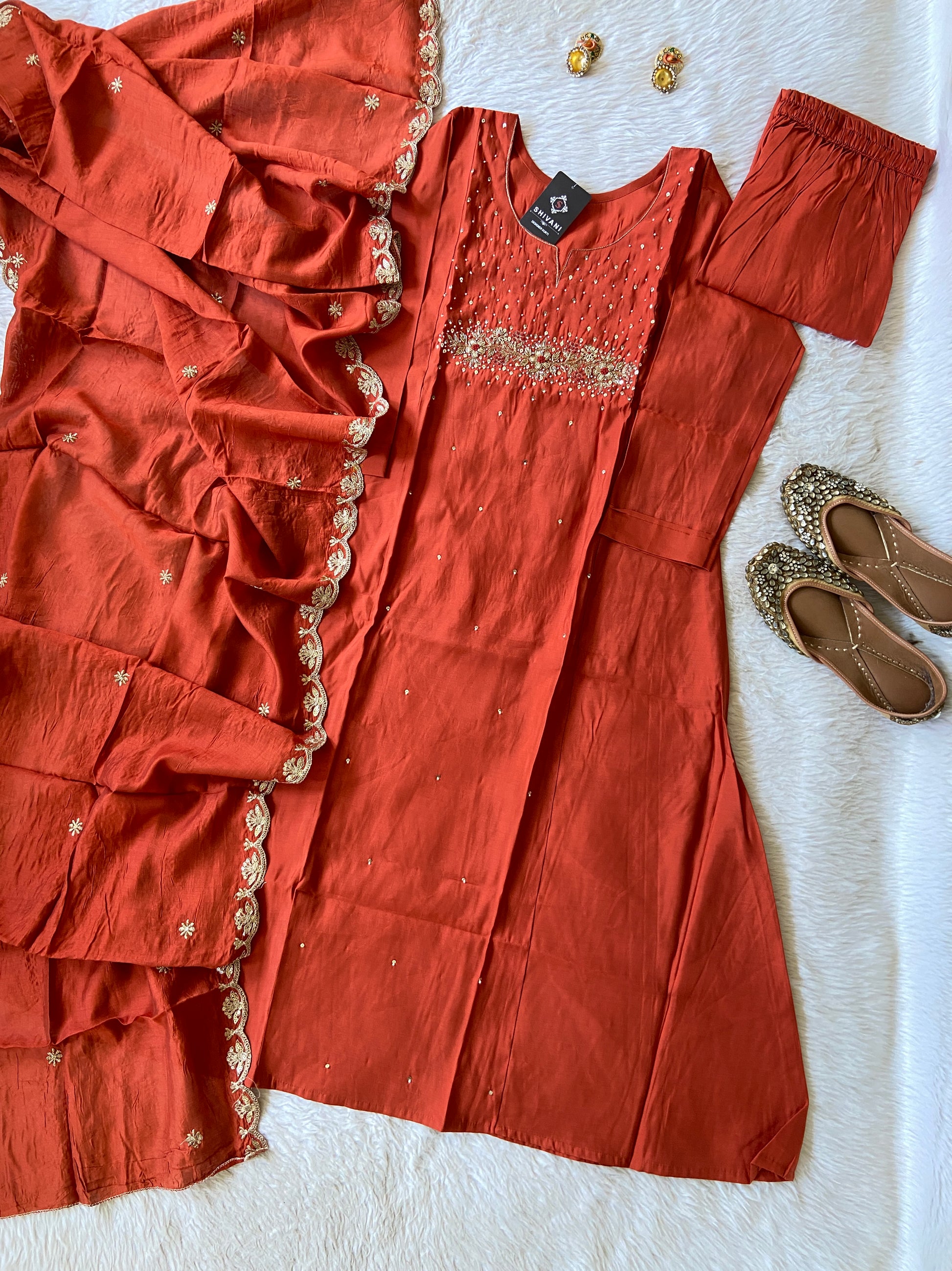 Red traditional outfit with matching dupatta, shoes, and earrings on a white surface