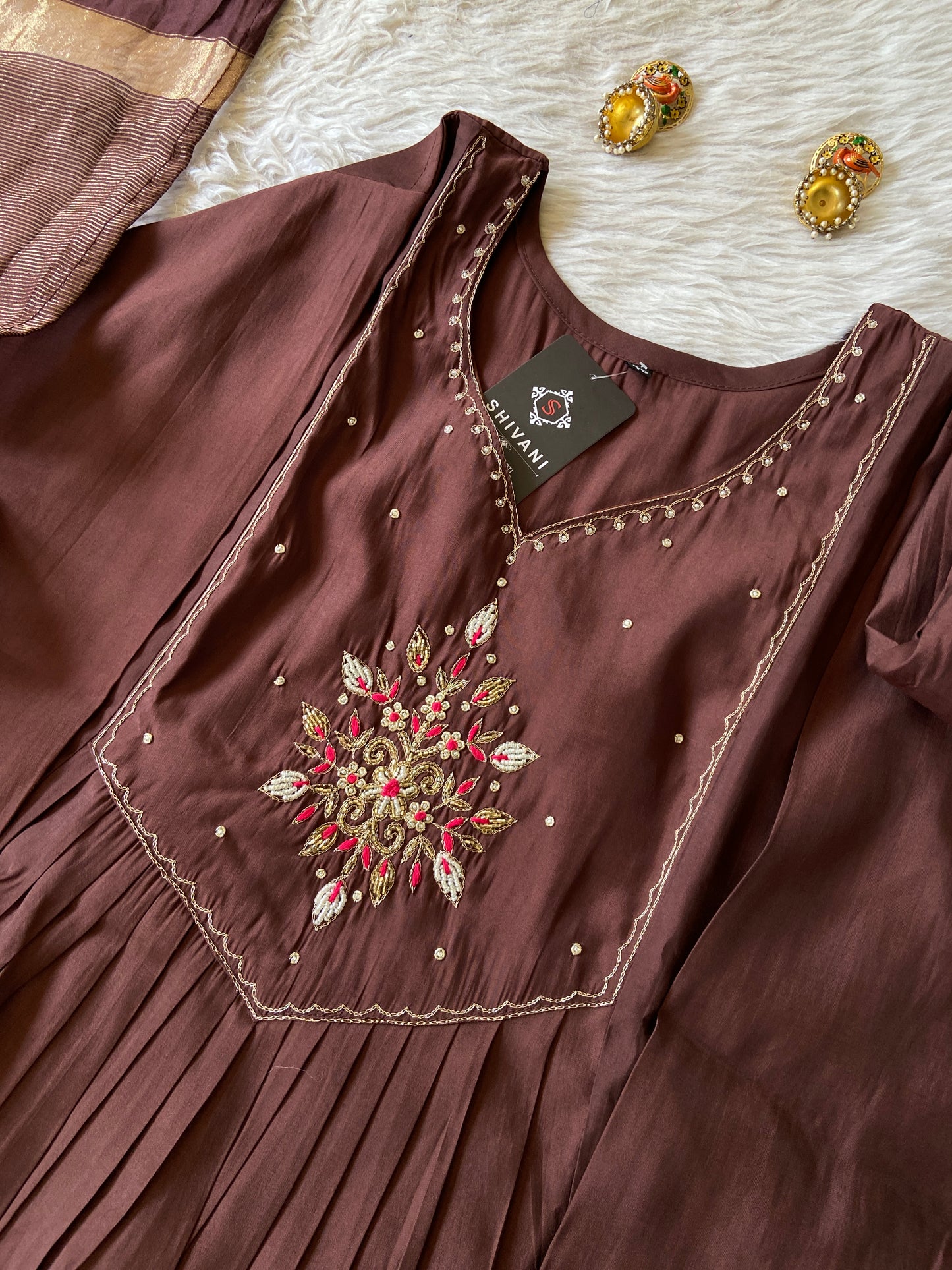 Brown dress with intricate embroidery and a tag on a textured surface