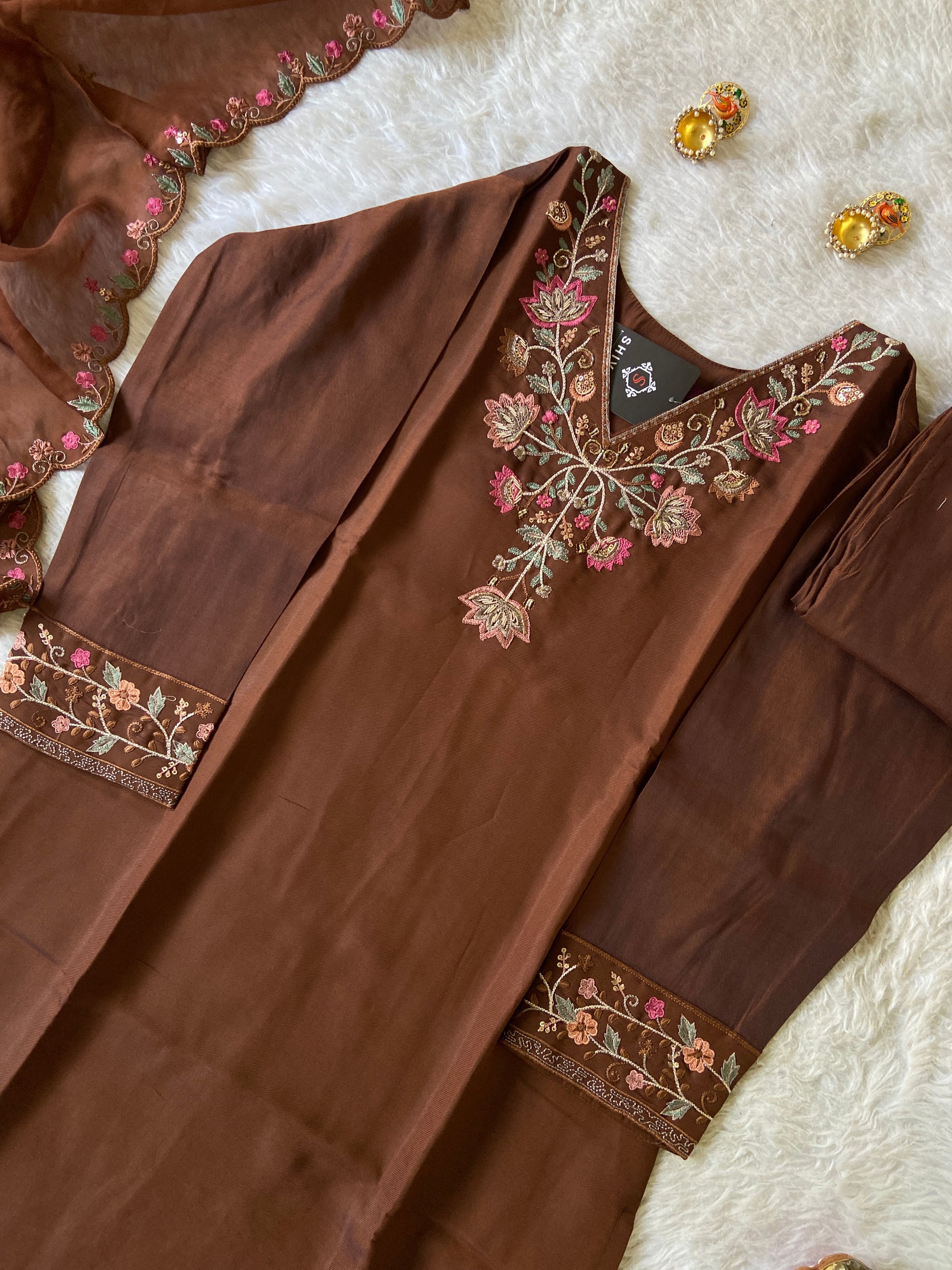 Brown embroidered garment on a white surface with earrings.