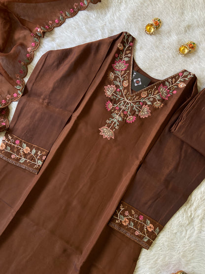 Brown embroidered garment on a white surface with earrings.