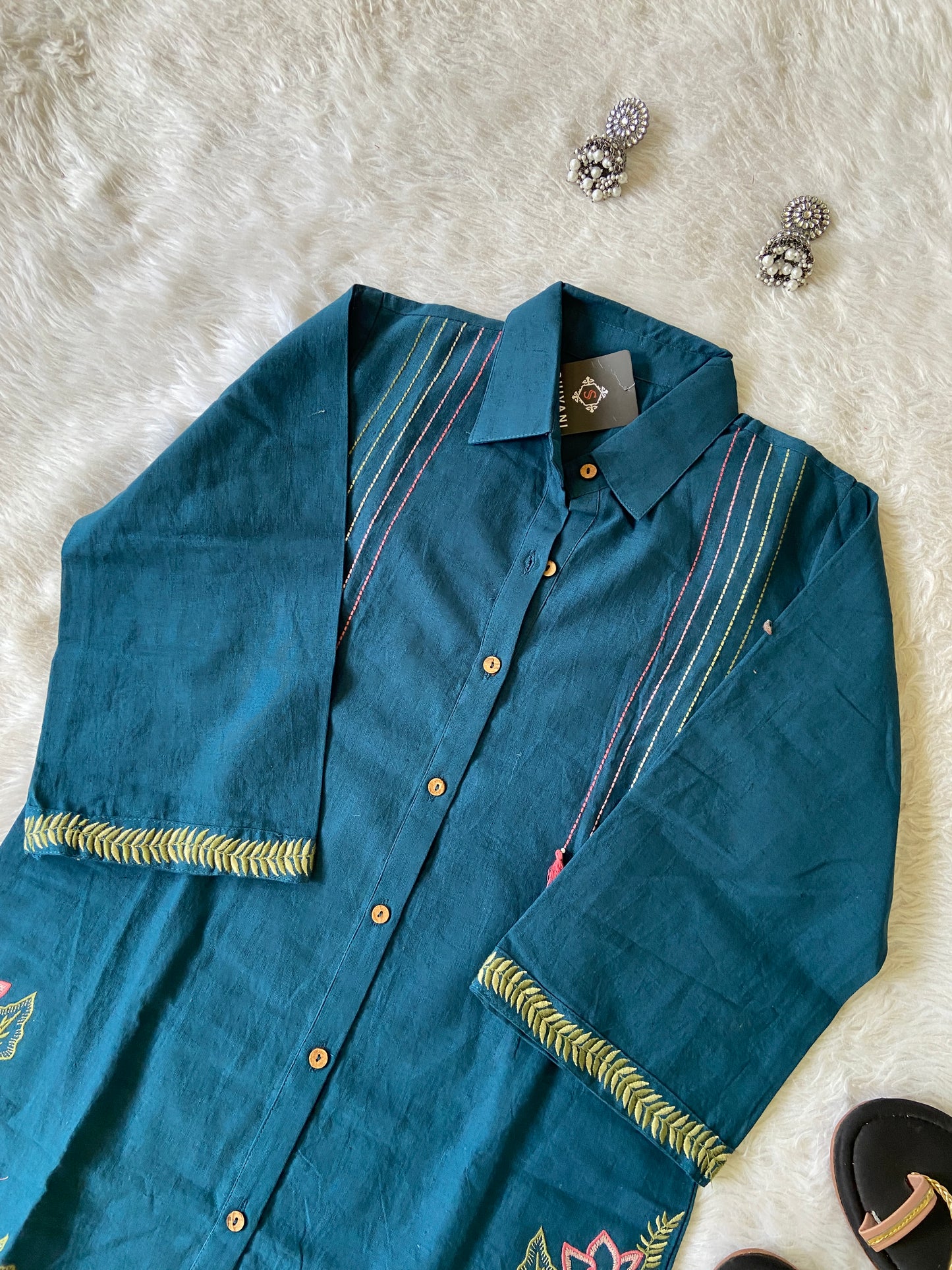 Blue embroidered shirt on a white textured surface with earrings and a box in the background