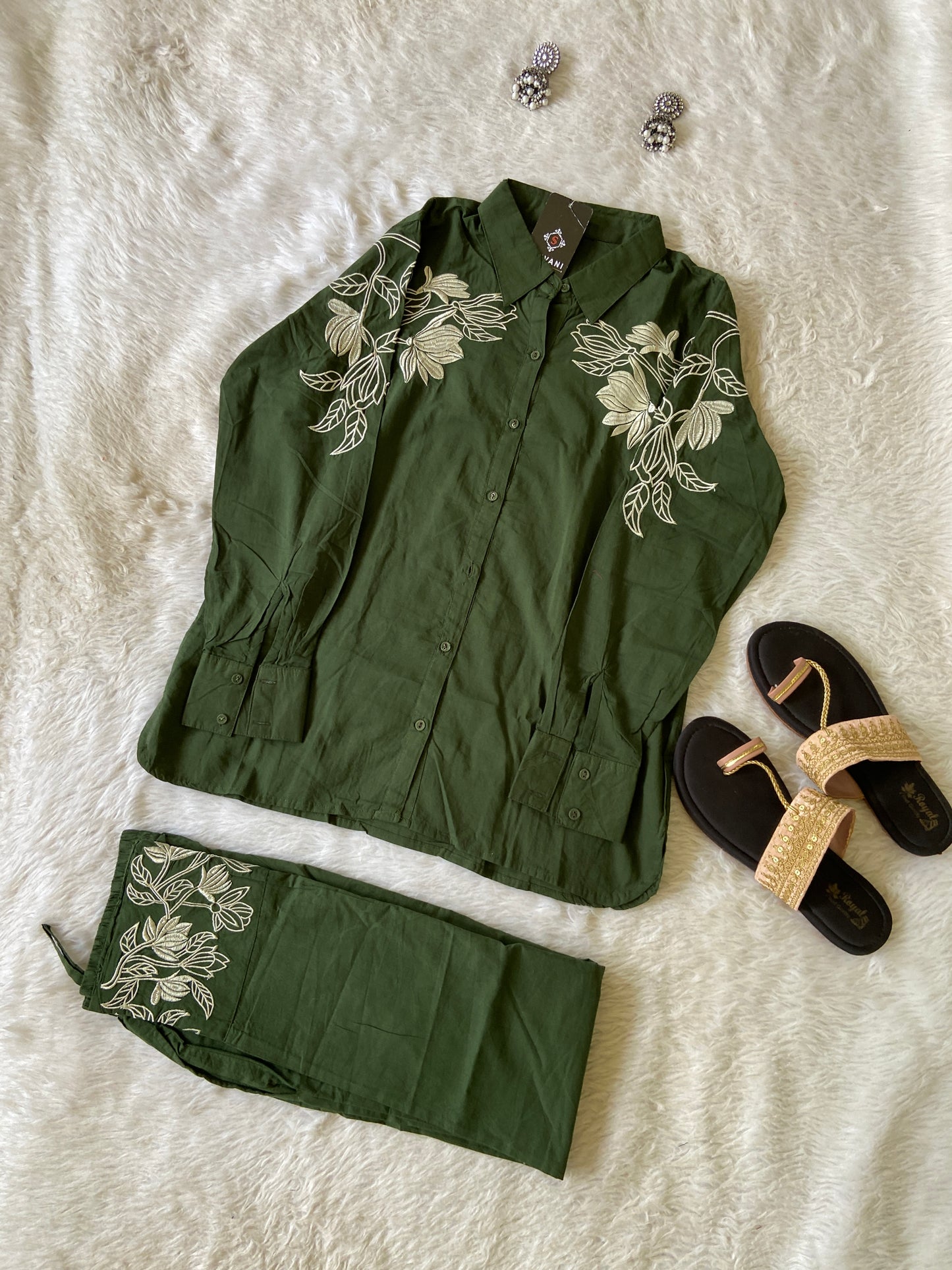Green embroidered outfit with sandals and jewelry on a textured surface