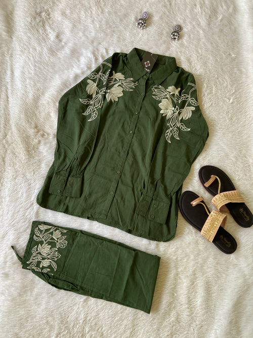 Green embroidered outfit with sandals and jewelry on a textured surface