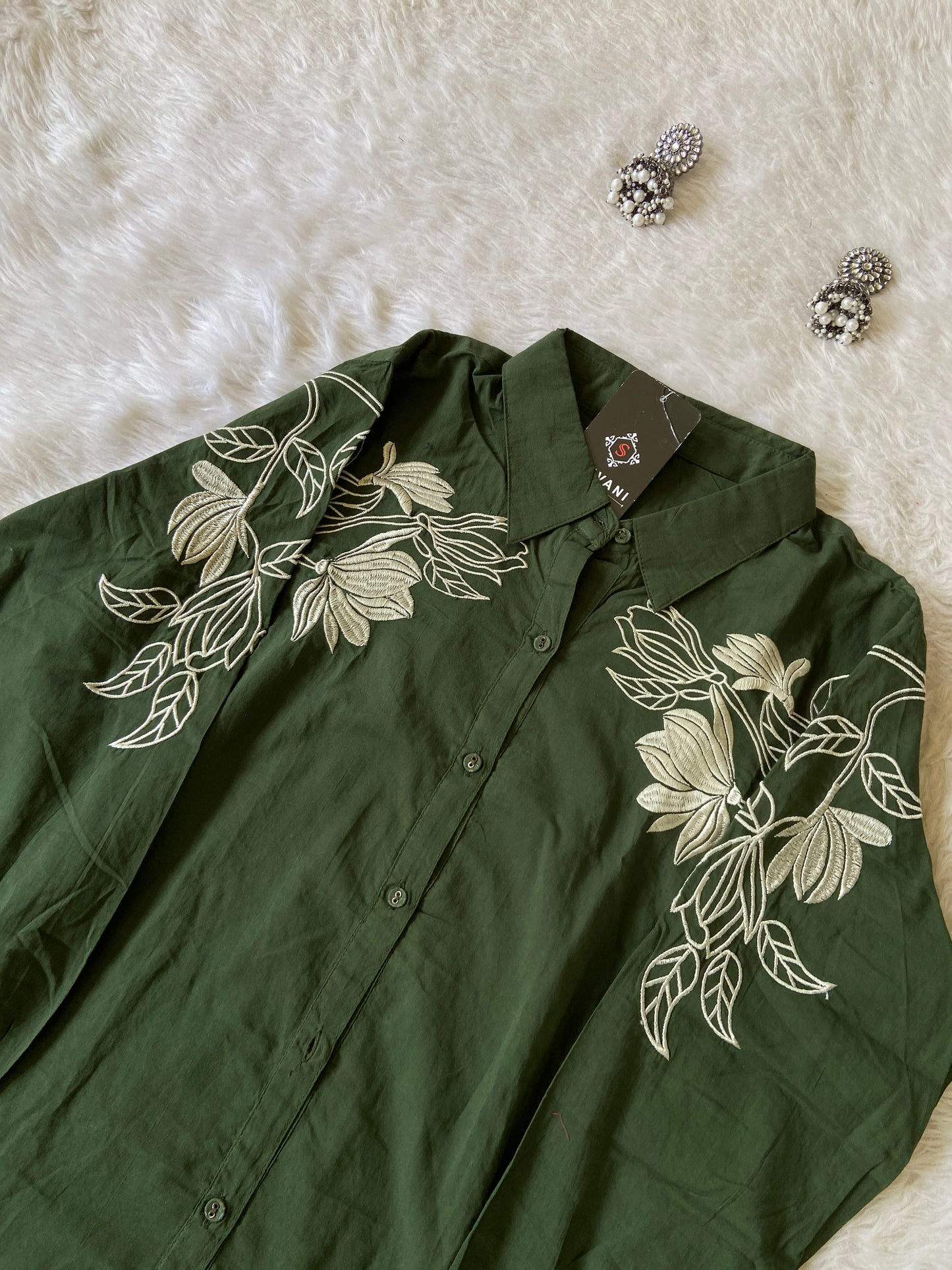 Green shirt with floral embroidery on a white fur surface