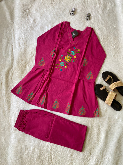 Pink embroidered outfit with floral patterns on a textured surface