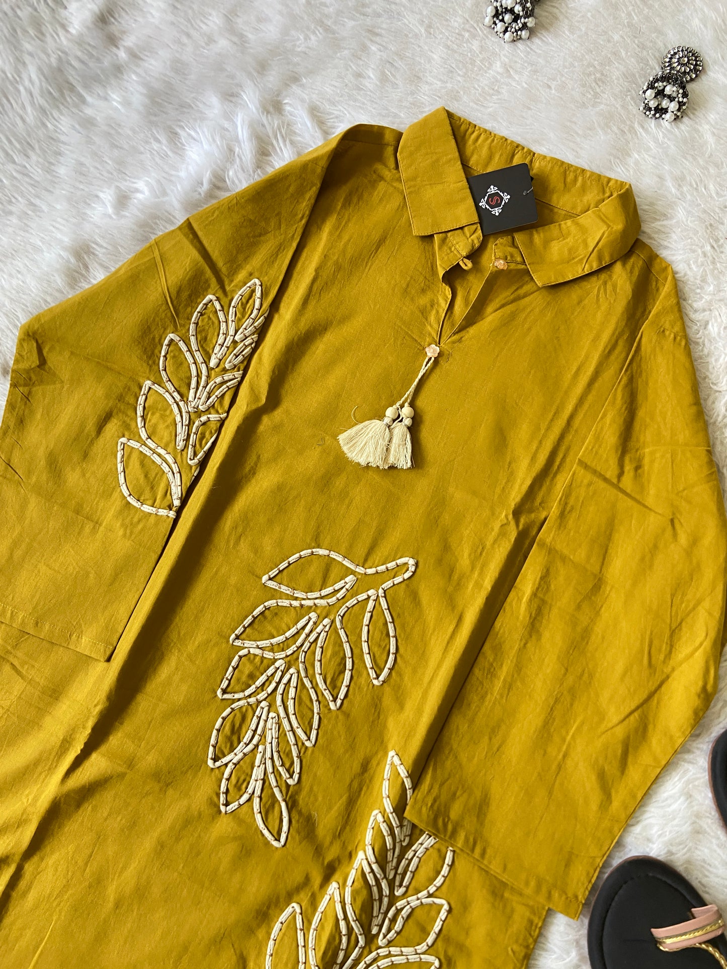 Mustard yellow shirt with leaf embroidery on a white surface