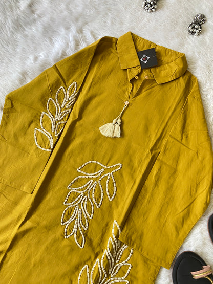 Mustard yellow shirt with leaf embroidery on a white surface
