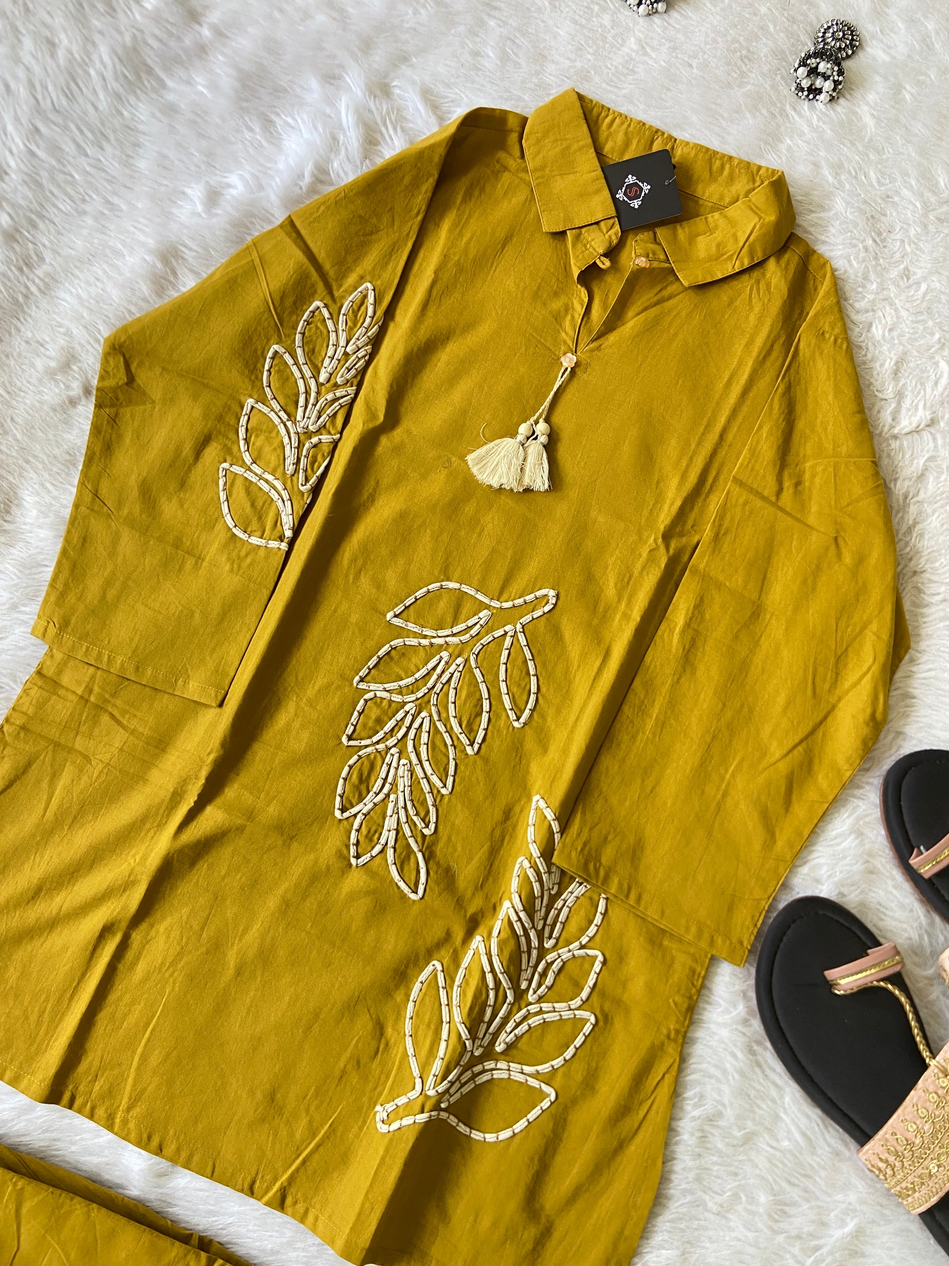 Mustard yellow garment with leaf embroidery on a white fur surface.