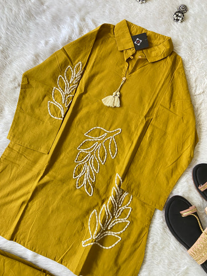 Mustard yellow garment with leaf embroidery on a white fur surface.