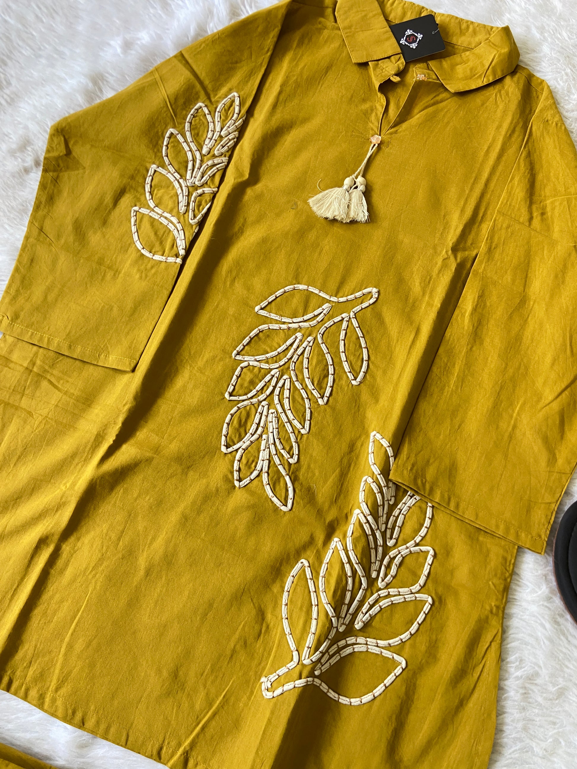 Mustard yellow shirt with leaf patterns on a white surface