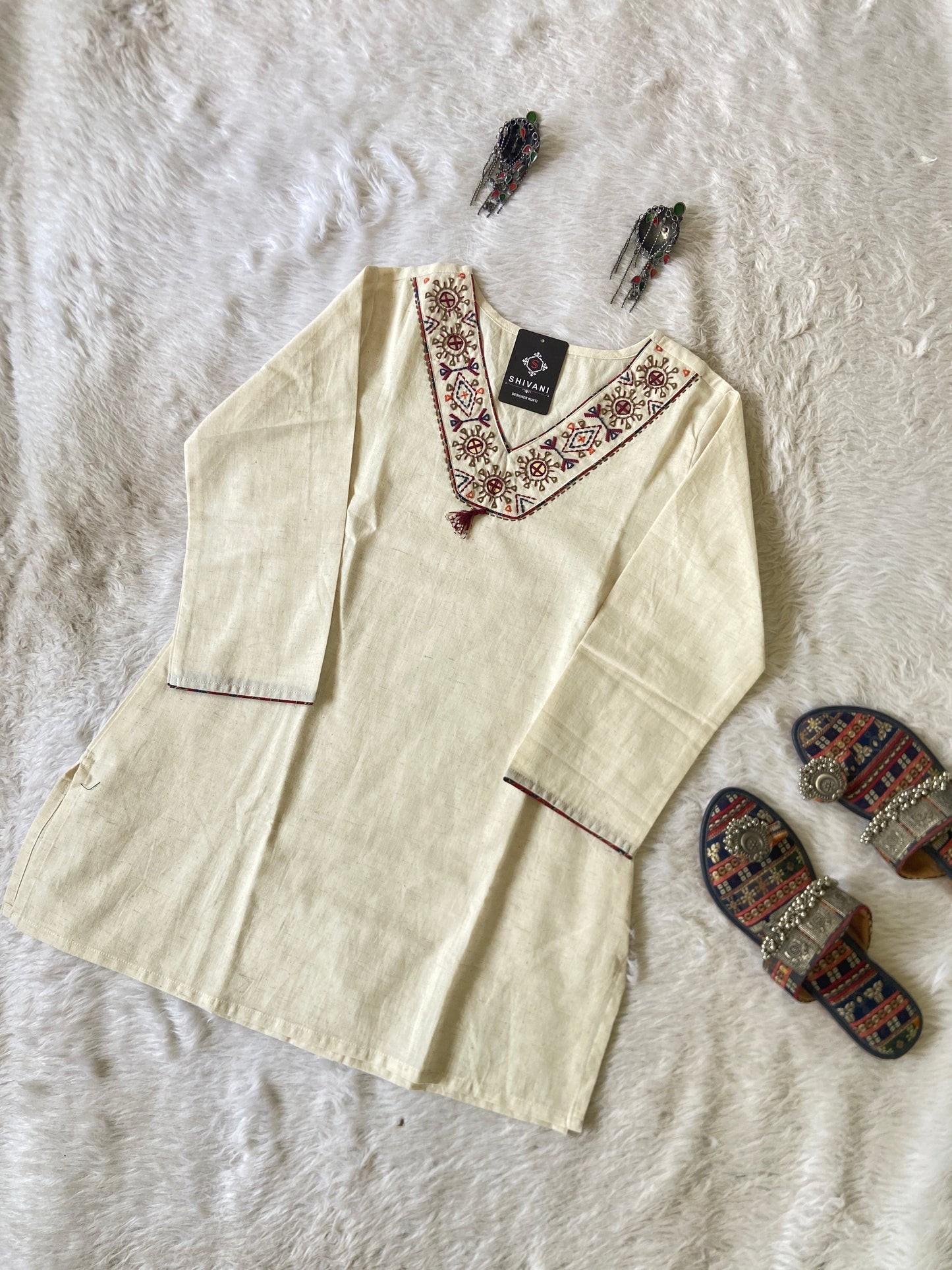 Beige embroidered shirt on a textured white surface with decorative slippers.