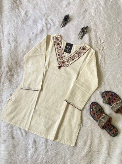 Beige embroidered shirt on a textured white surface with decorative slippers.