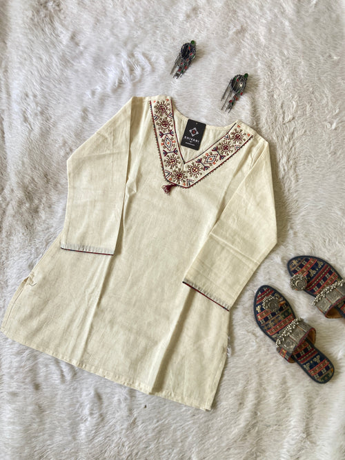 Beige embroidered shirt on a textured white surface with decorative slippers.