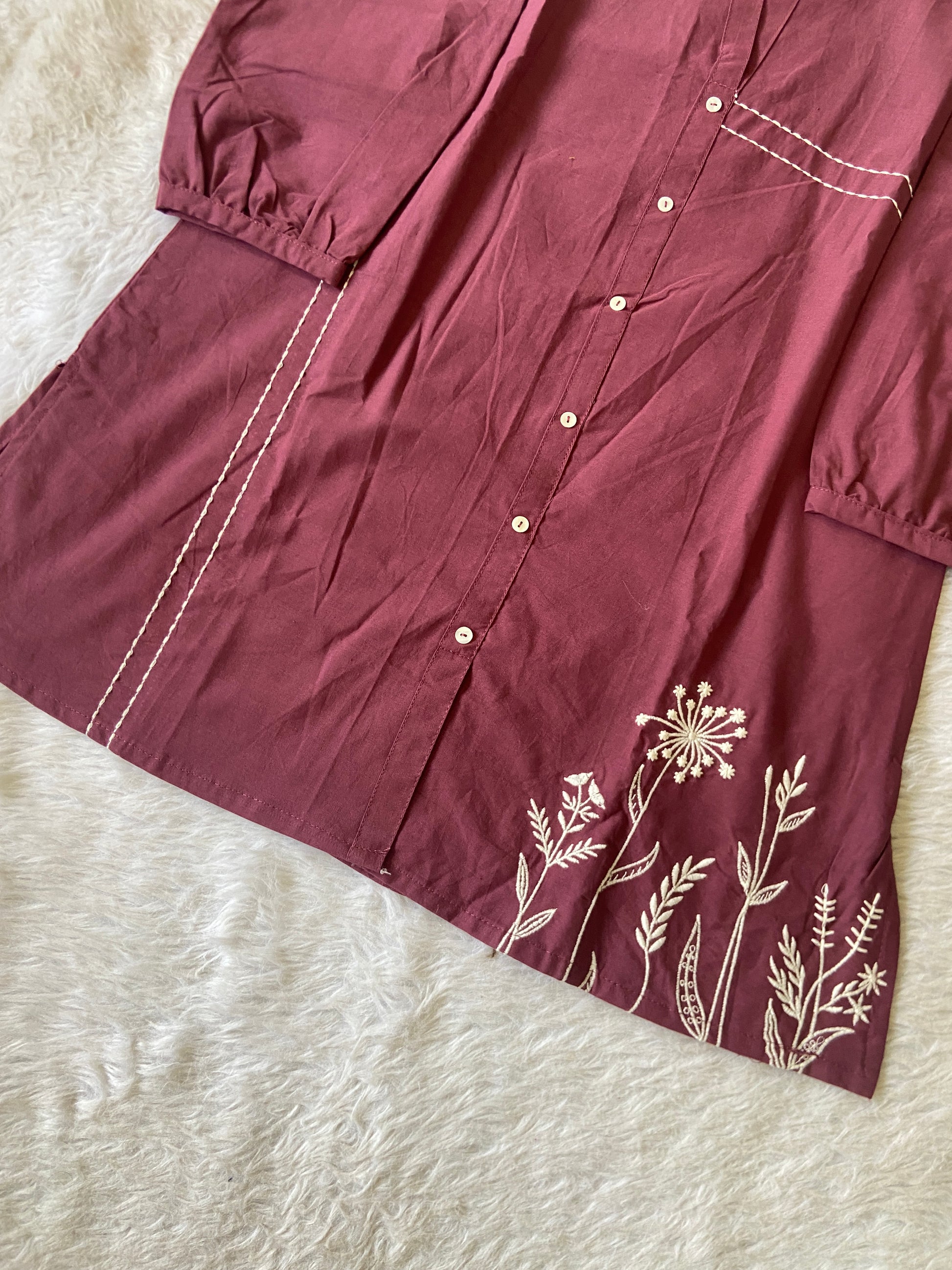 Maroon fabric with white floral embroidery on a white fur background