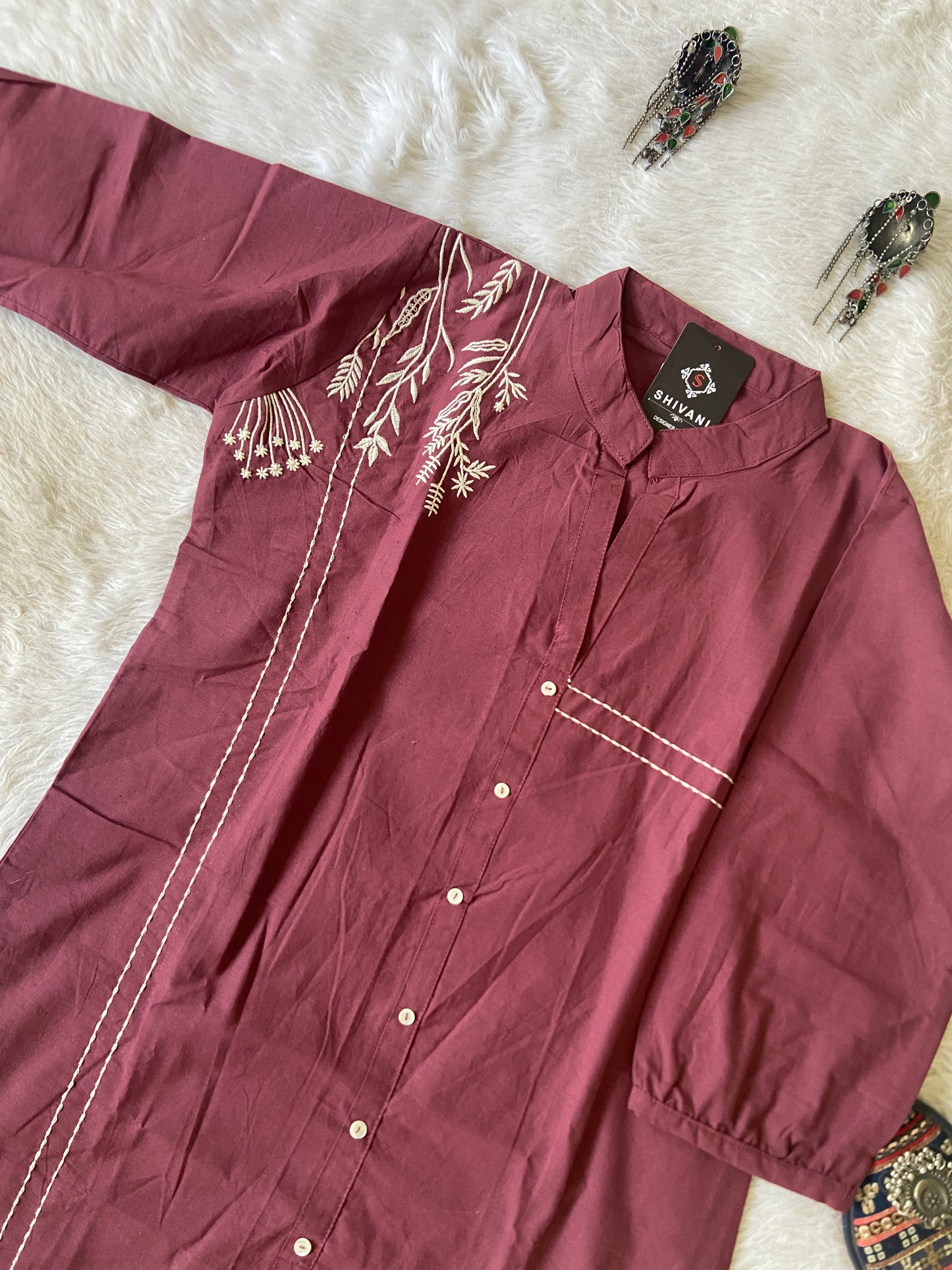 Maroon shirt with white embroidery on a white surface